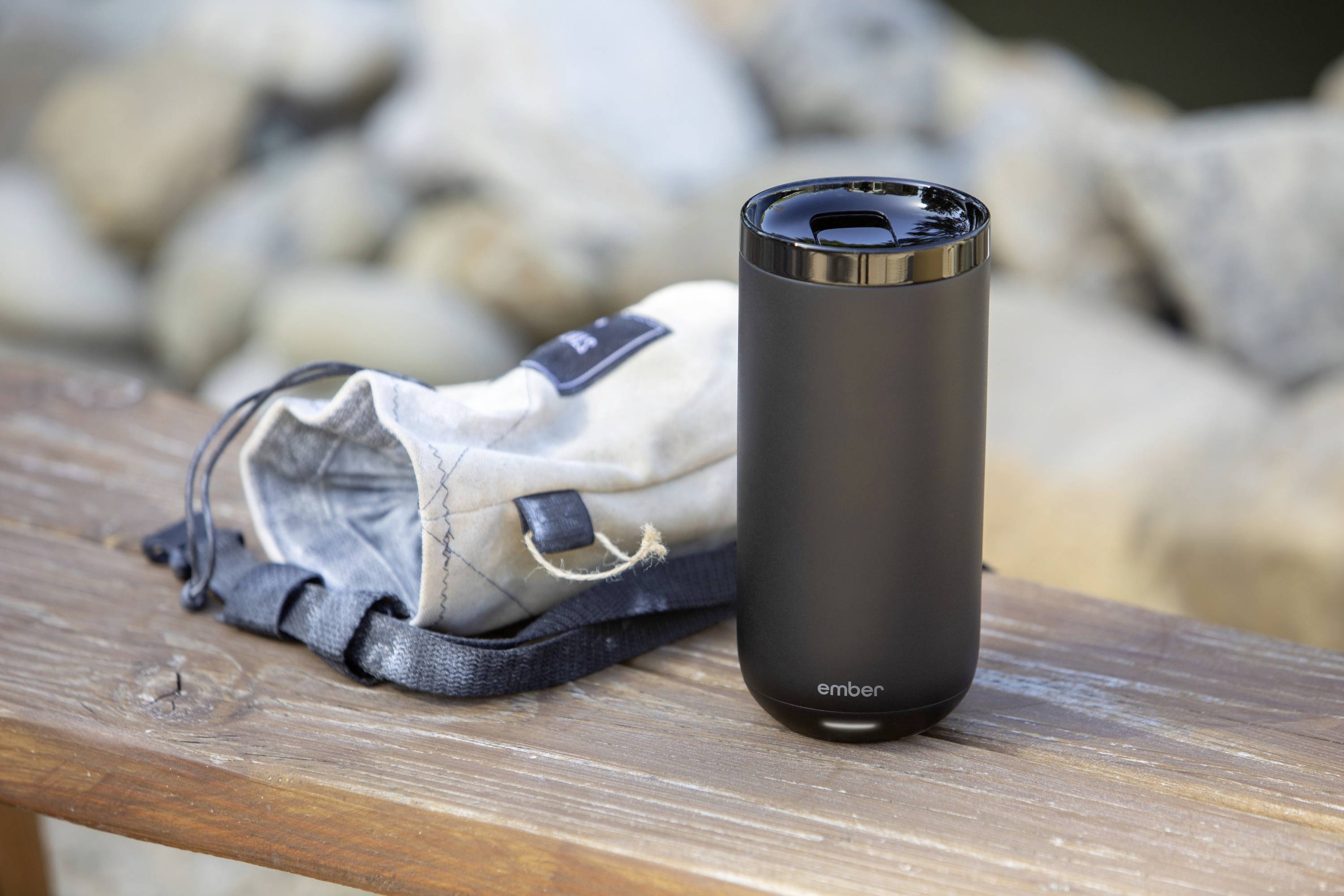 Black drinking cup with detachable bag on a wooden bench outdoors.