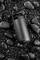 A black thermal mug rests on smooth, dark stones.