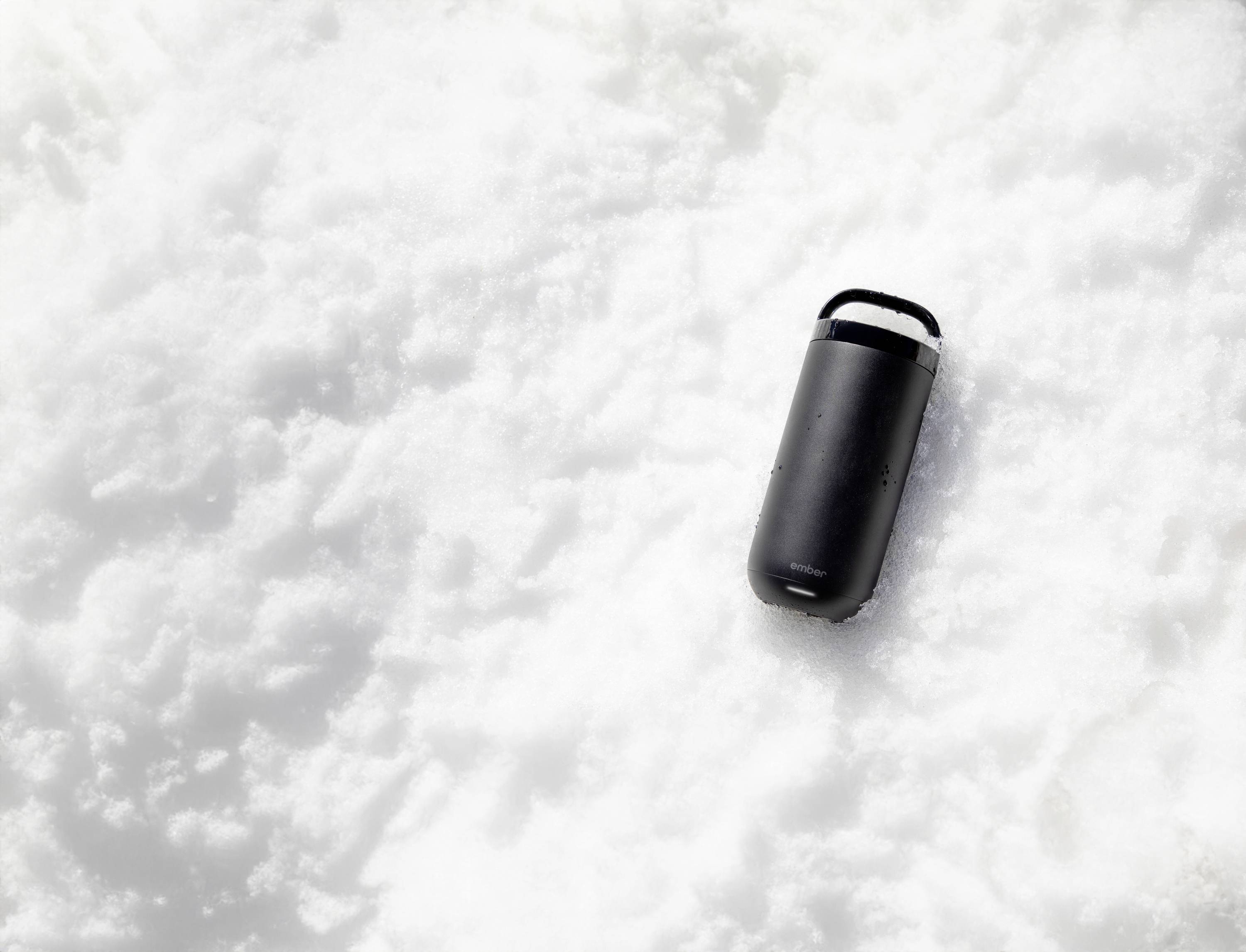 A black coffee mug lies in the snow.