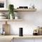 Modern kitchen with shelves displaying plants and books. A coffee machine and a black speaker sit on the worktop.