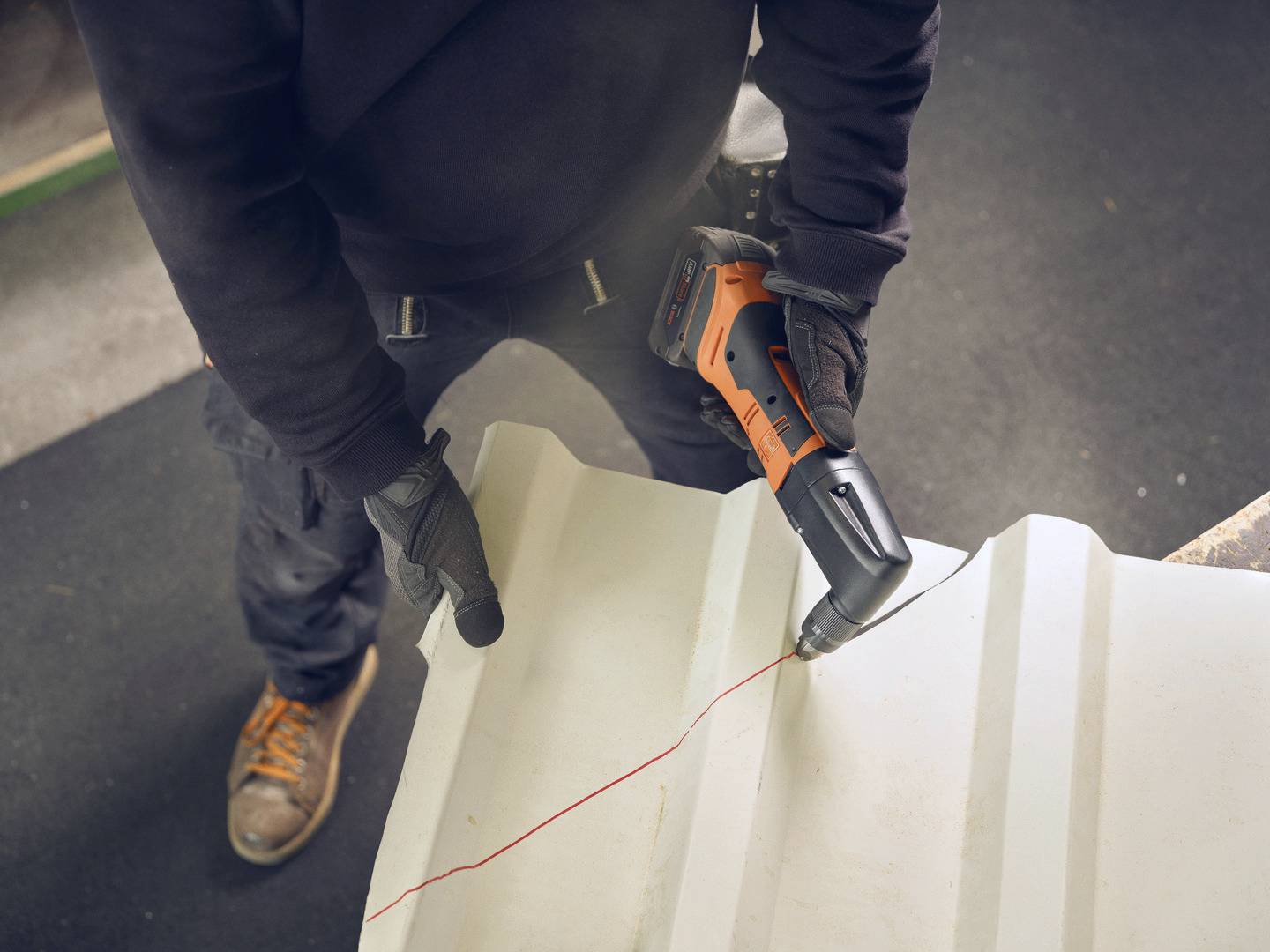 A person is cutting along a red line on a large white plastic material using an electric saw.