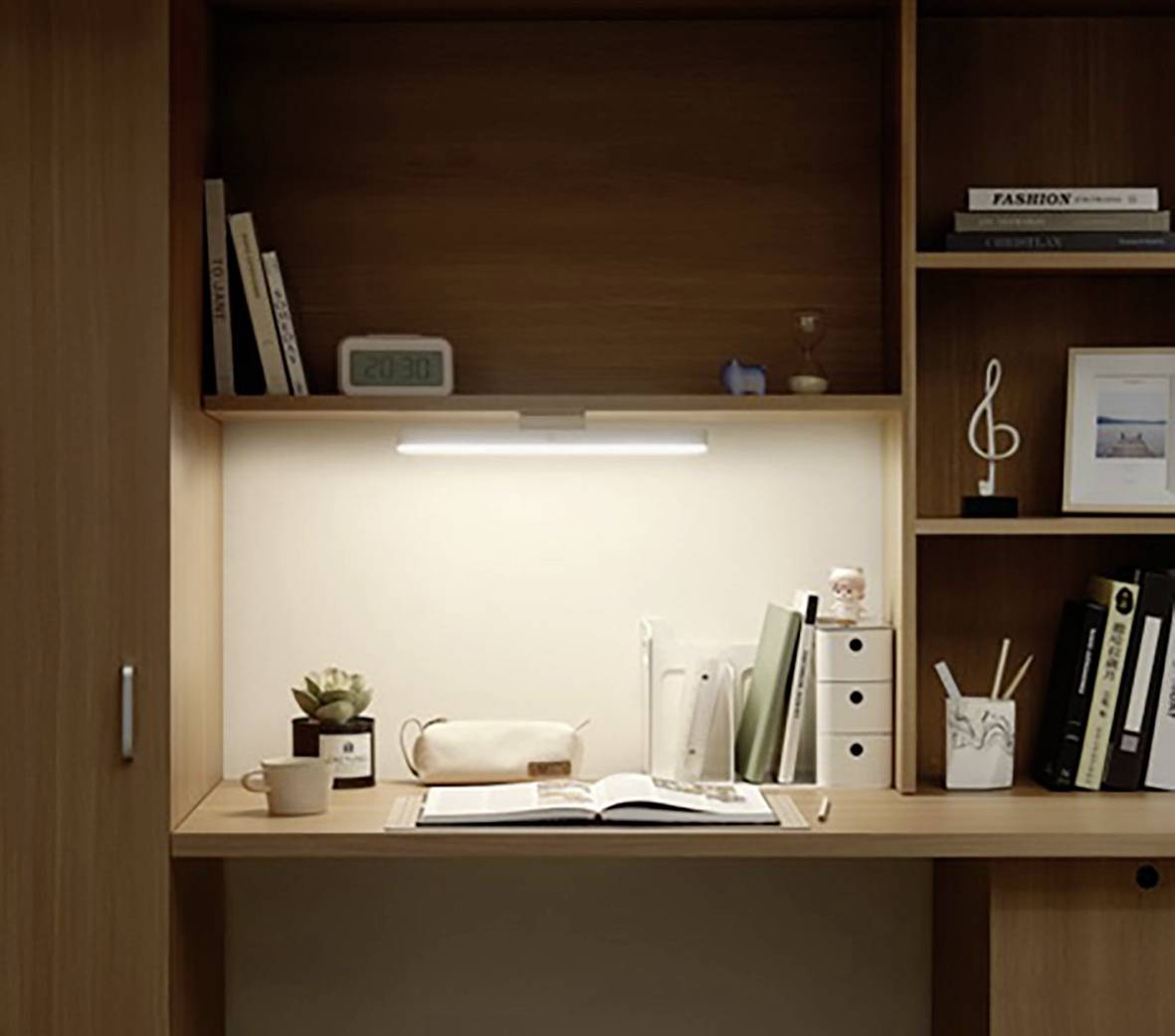 A wooden desk with an open book, pen holders, and a plant. Bookshelves with books, a clock, and decorations in the background.