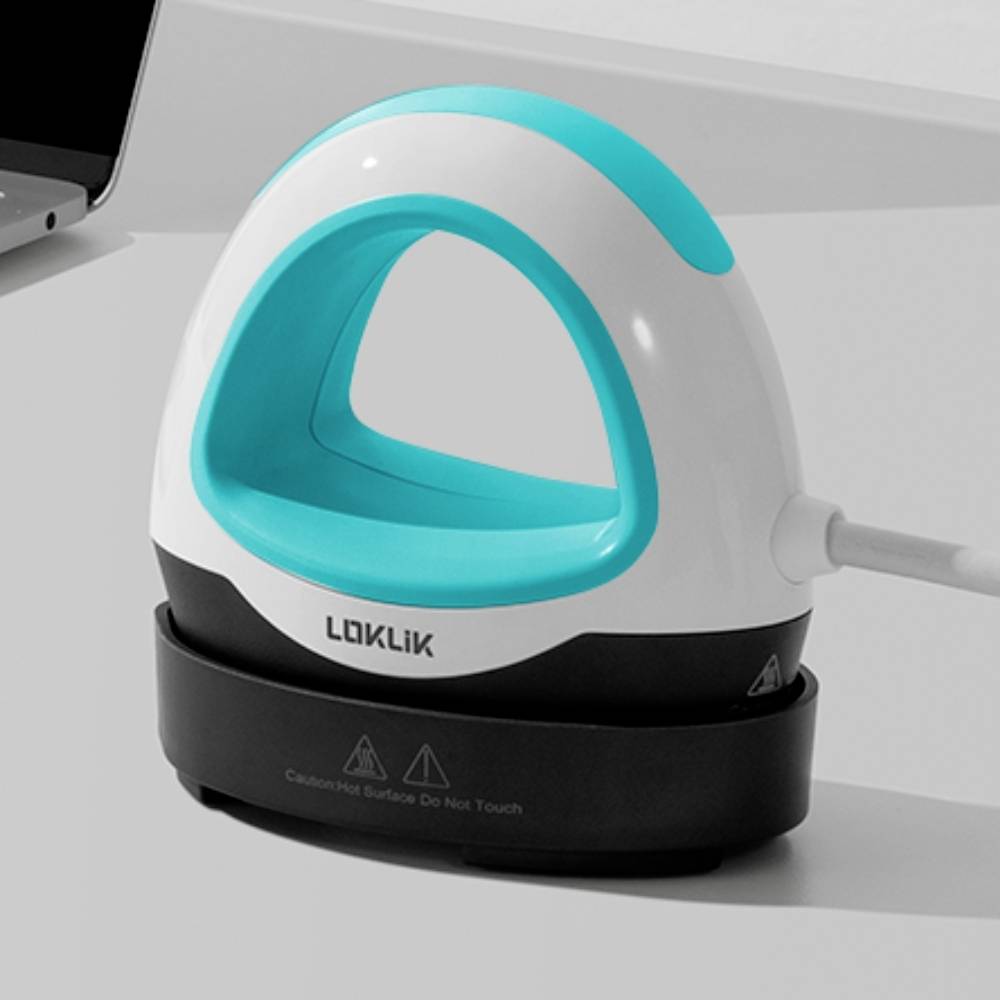 A white and blue iron on a charging station, with the 'LOKLIK' branding clearly visible at the front. It is positioned next to a laptop.