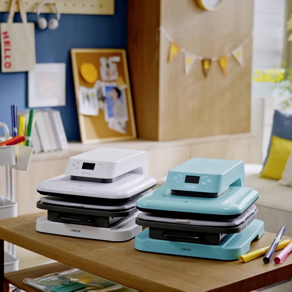 Two modern printing machines, one in white and one in turquoise, stand on a table in a creatively designed workspace.