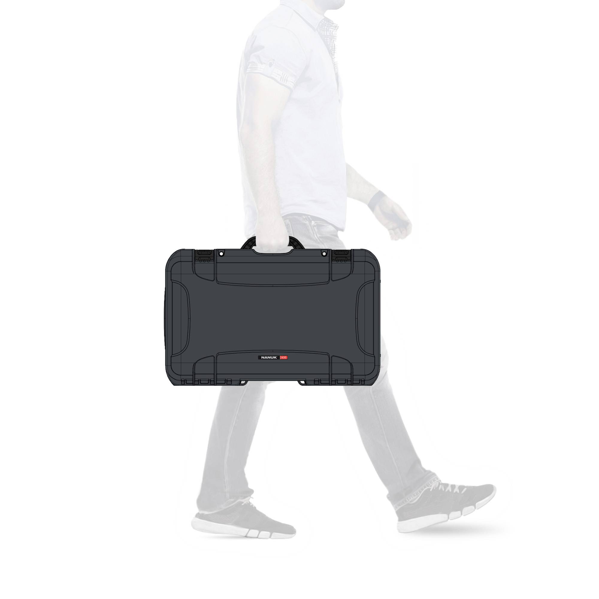 A person wearing jeans and a T-shirt is carrying a black suitcase in their hand. The focus is on the suitcase.