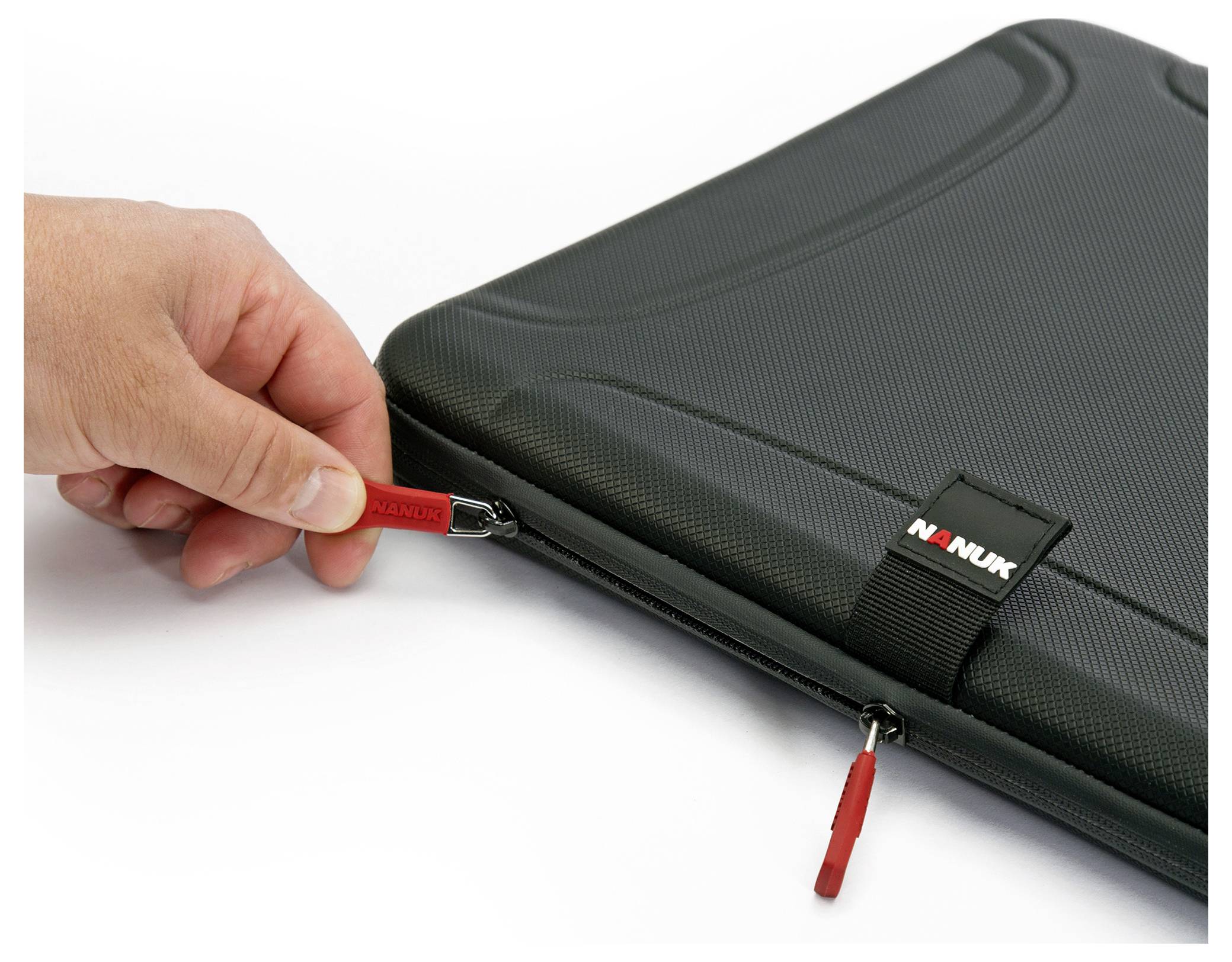 A hand opens the zip of a black, robust Nanuk case with red tags.