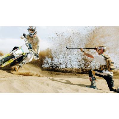 A motorcyclist rides through sand, kicking up dust, while a photographer captures him with an action camera to obtain a dynamic sports shot.