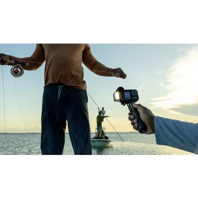 A person is holding a camera filming an angler on a boat at sunset.