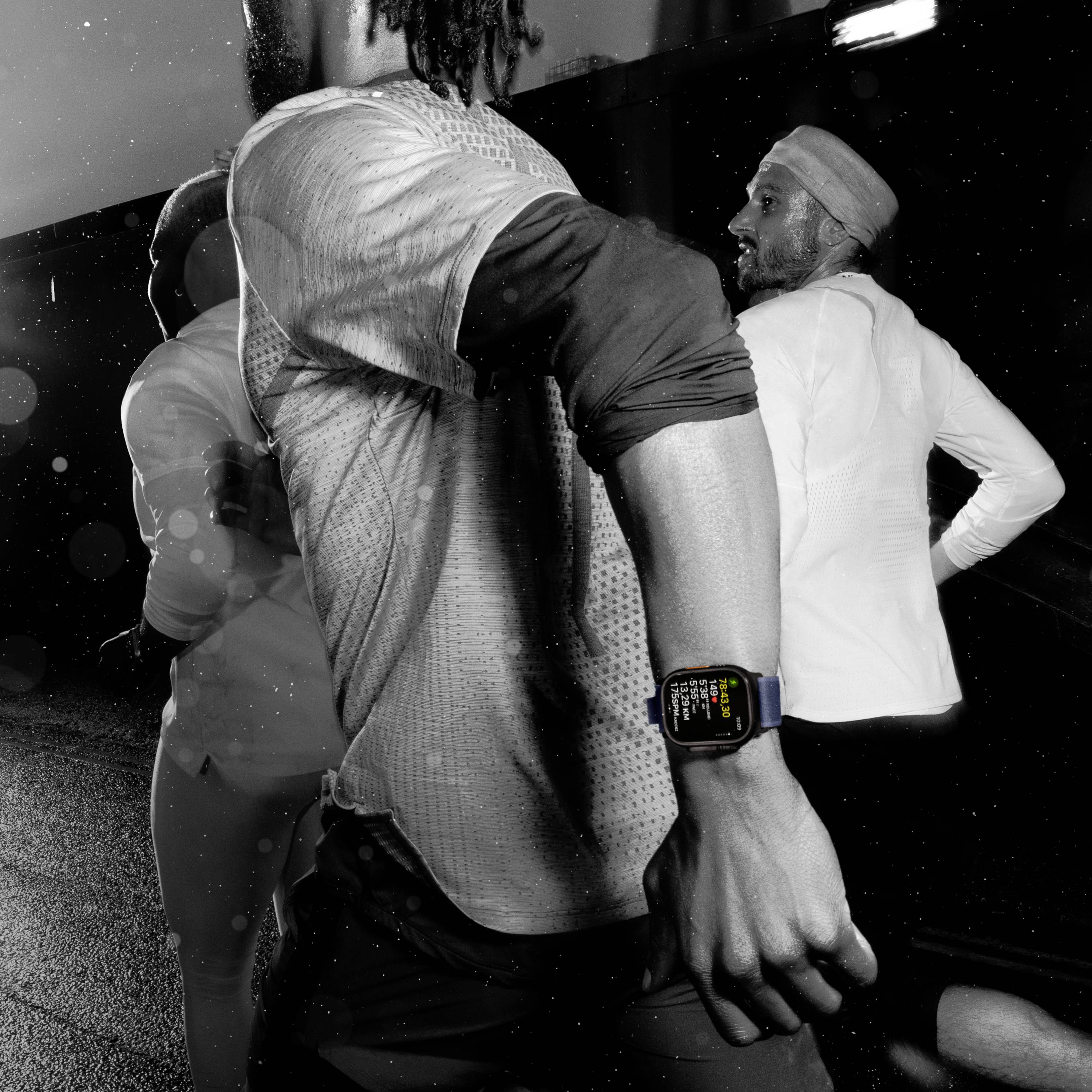 A group of people are running at night. One person is wearing a smartwatch that displays colourful symbols and information.