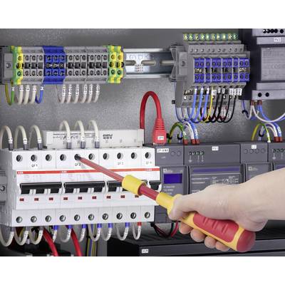 A person is working with a screwdriver on a control panel with numerous electrical circuits and coloured cables.