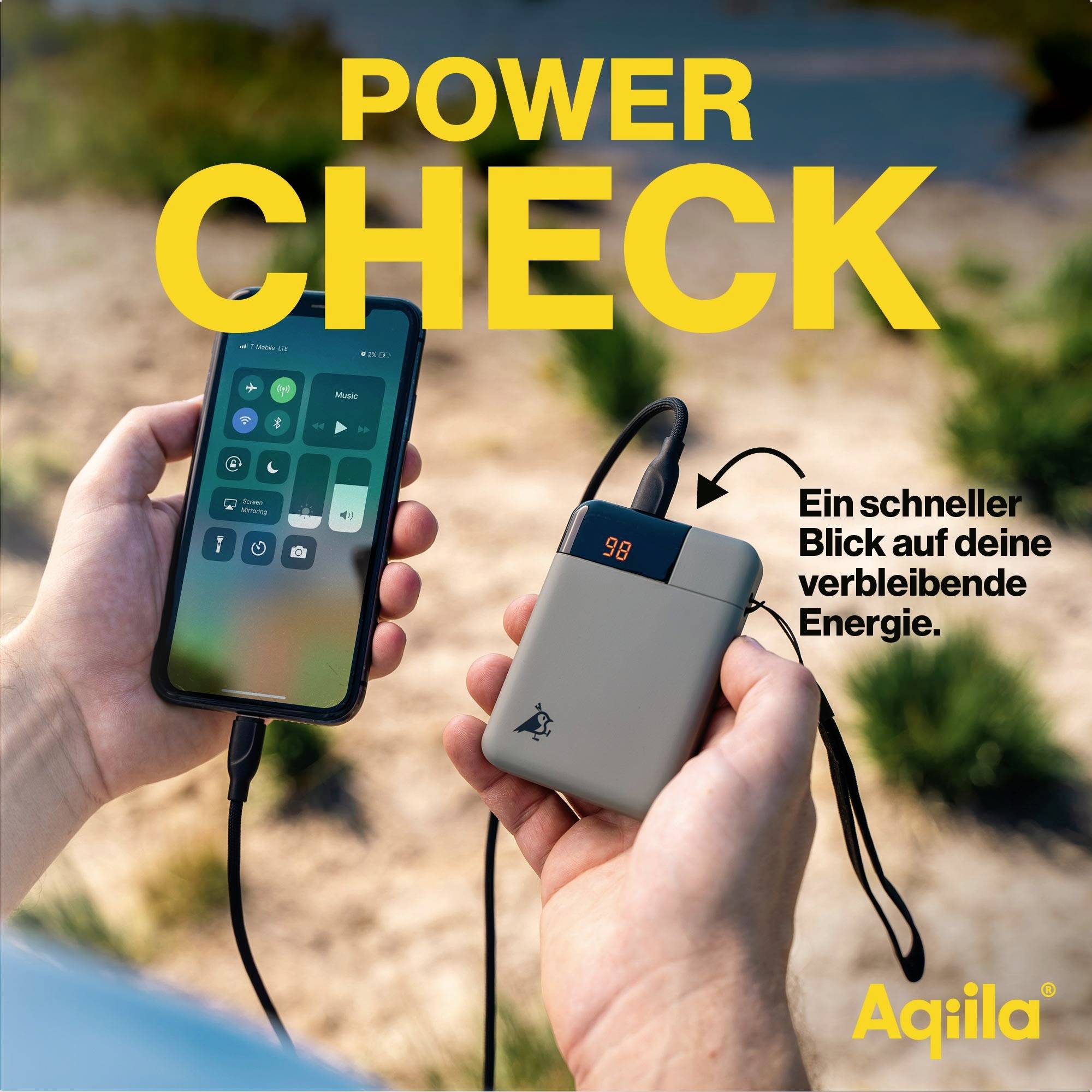 Two hands holding a smartphone and a power bank outdoors. The power bank displays 98% charge. Text: 'A quick glance at your remaining battery.'