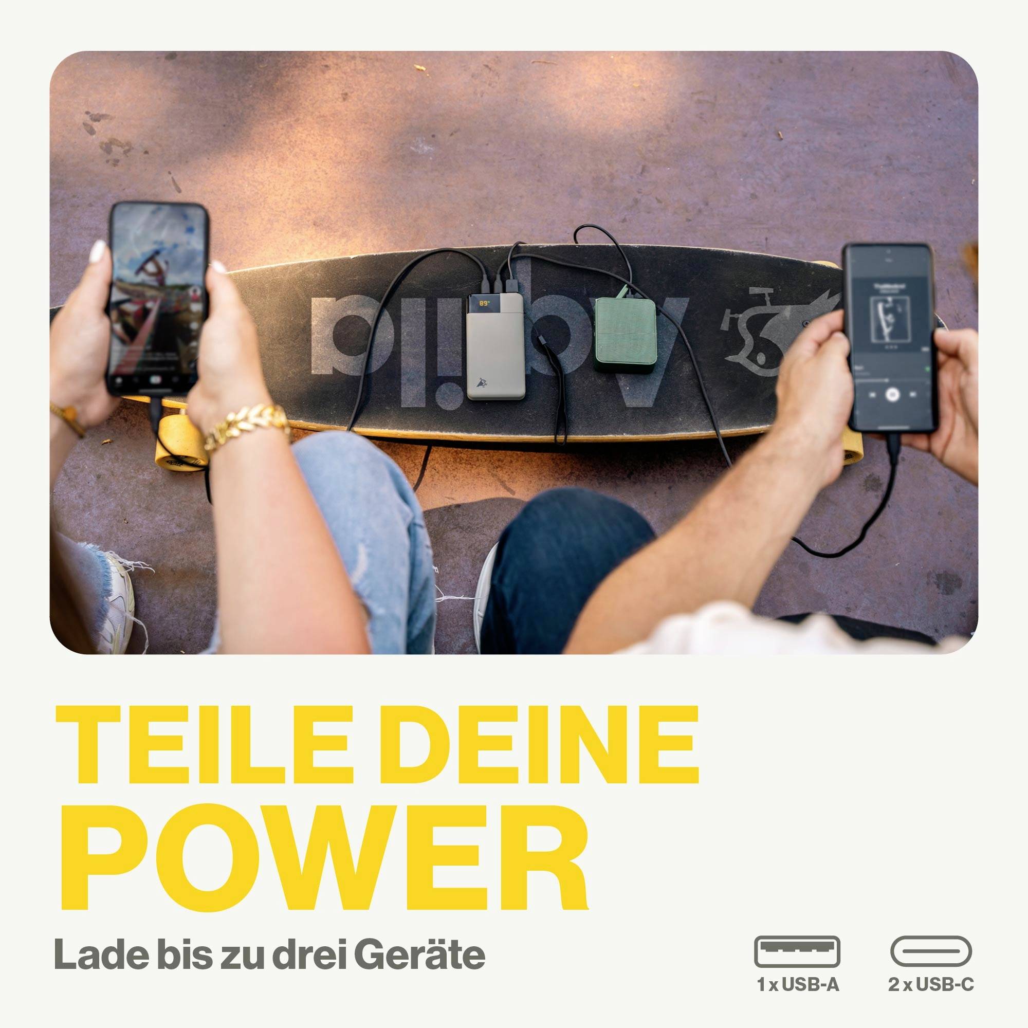 Two people are charging their devices with power banks resting on a skateboard. Text: 'Share your power. Charge up to three devices'.