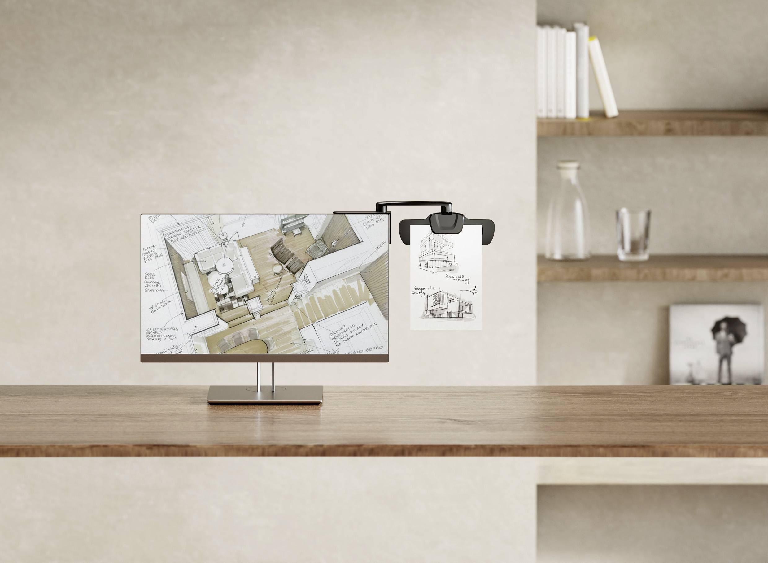 A monitor on a table displays floor plan sketches of a room, with a similar paper drawing hanging beside it in a clip holder.