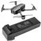 A black drone with four rotors hovers above a table. Underneath lies a large rectangular battery with labelling.