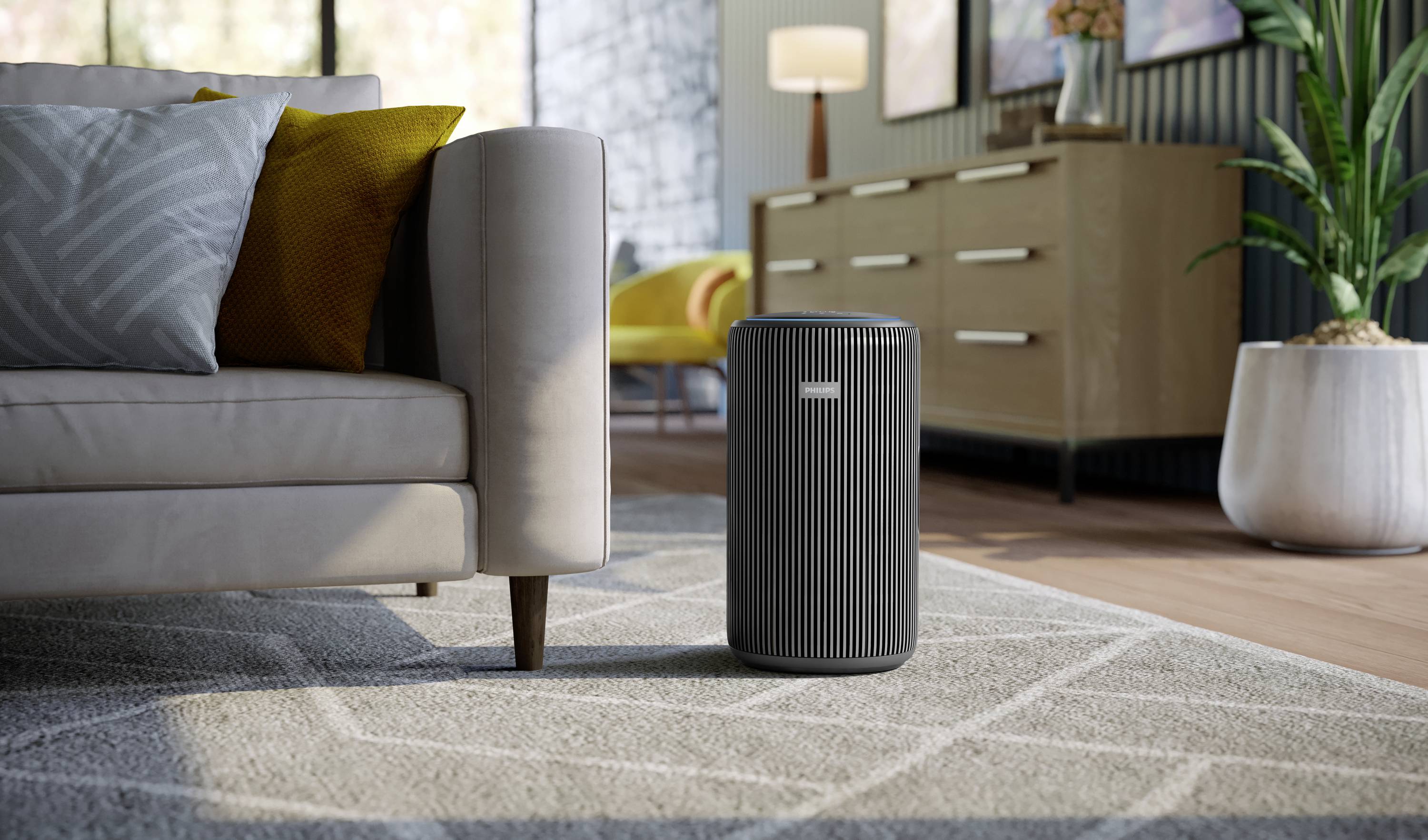 An air purifier stands on a carpet in the living room, next to a light-coloured sofa with colourful cushions; a chest of drawers is in the background.