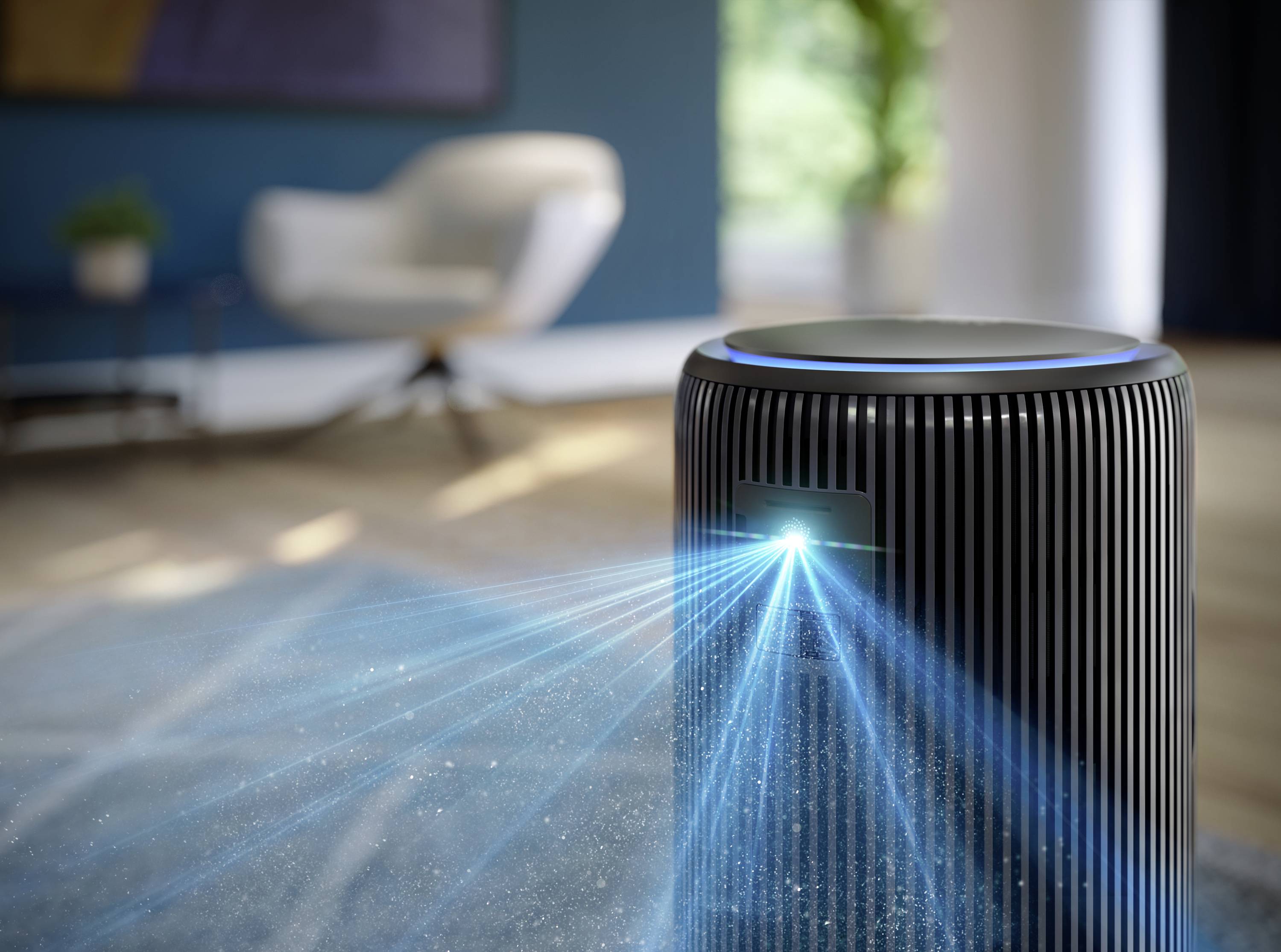 Air purifier in a modern room, emitting light rays and showing particles in the air. A blurred armchair in the background.