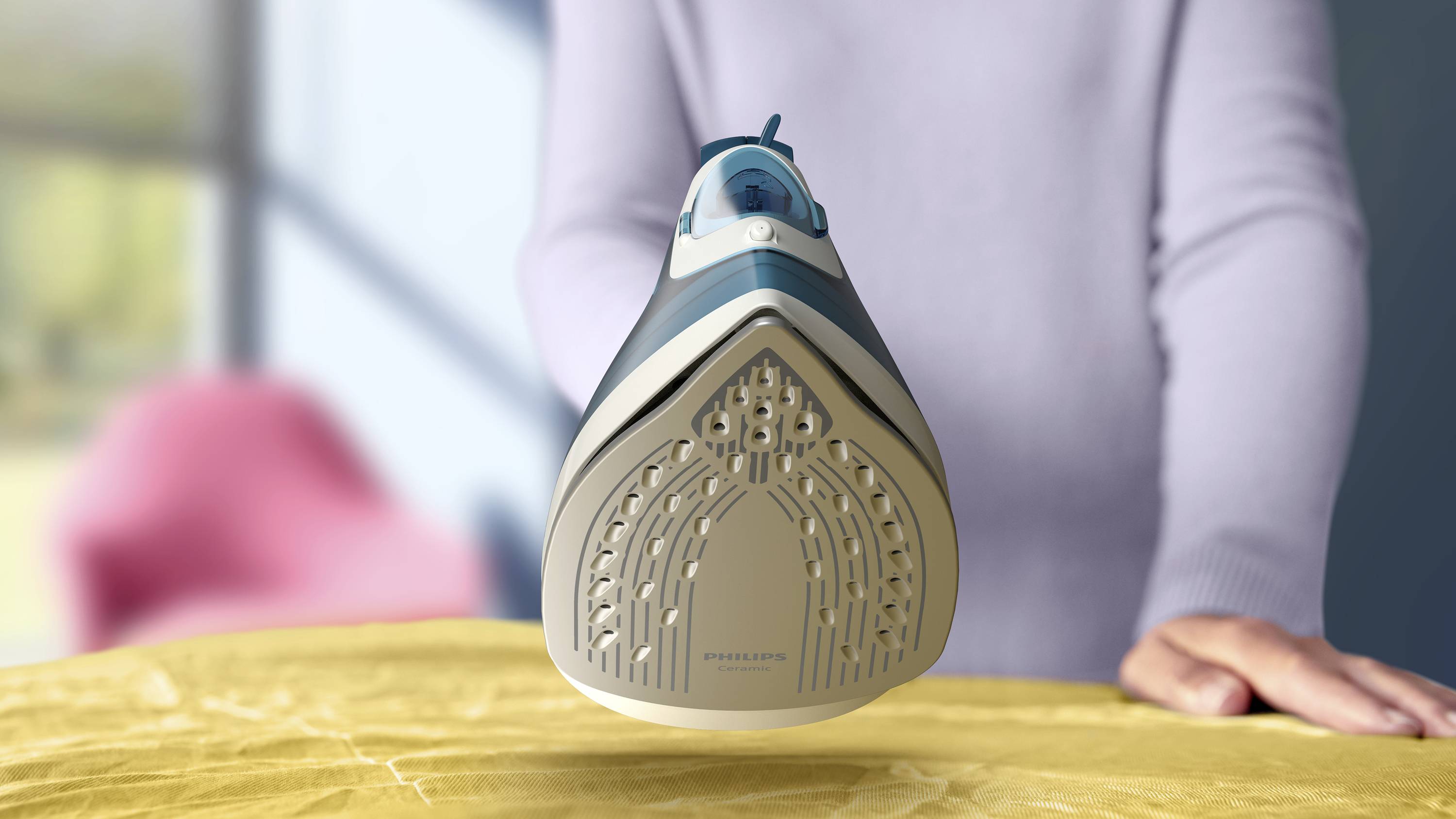 A person is ironing a yellow cloth with an iron. The iron is being held facing forward. A window is visible in the background.