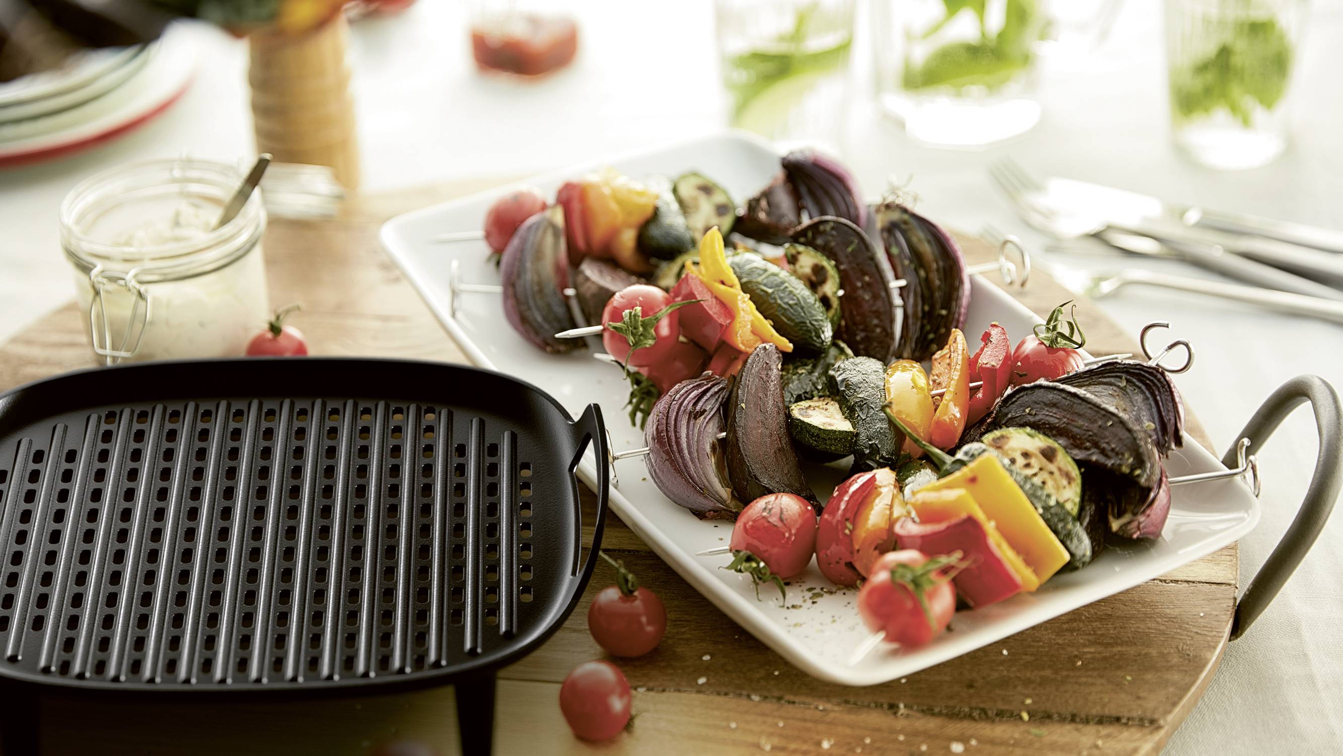 Grilled vegetables on a white plate: courgettes, peppers, cherry tomatoes and red onions. Alongside a griddle pan.