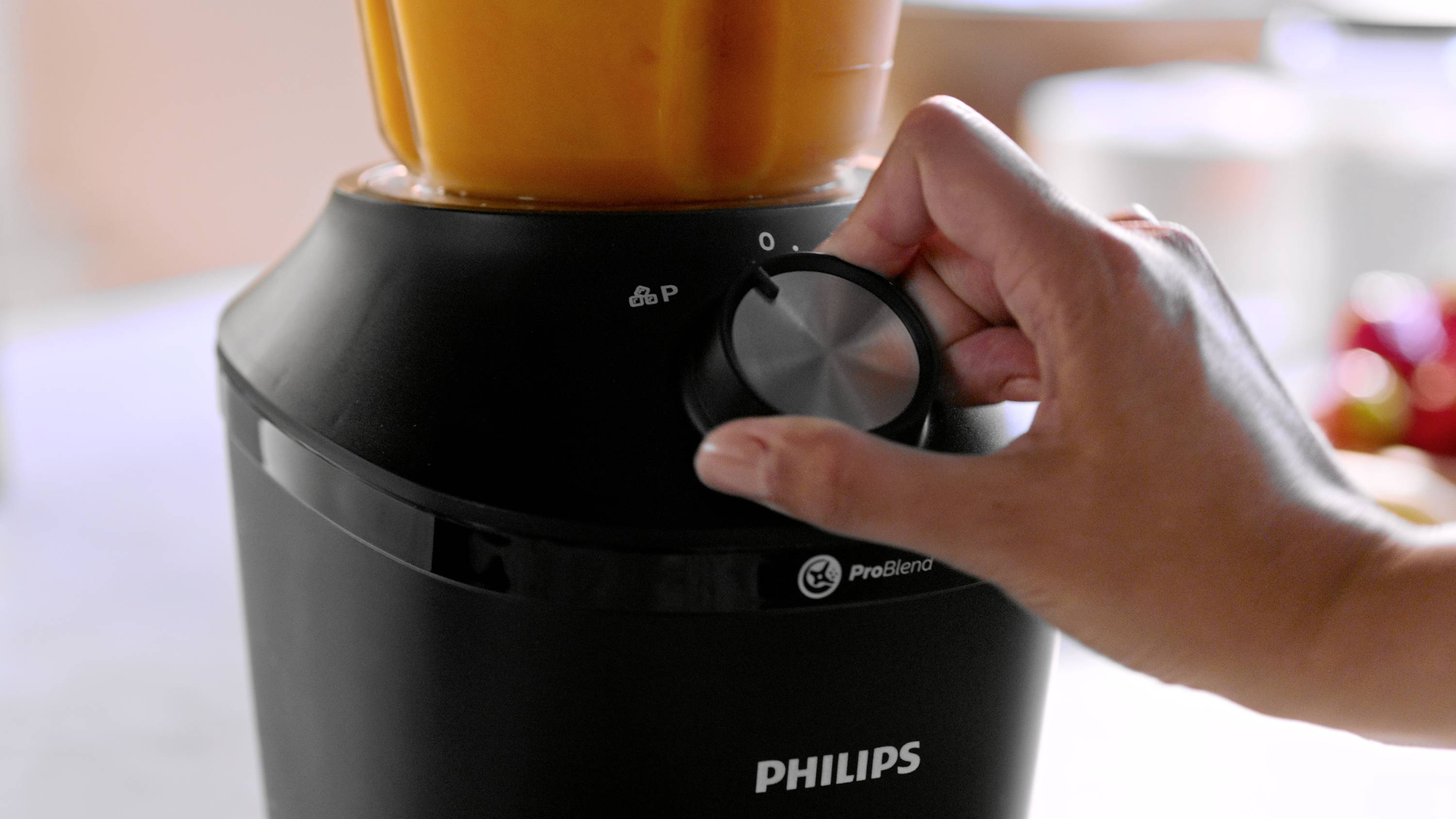 A hand turns the speed dial of a black mixer with an orange contents.