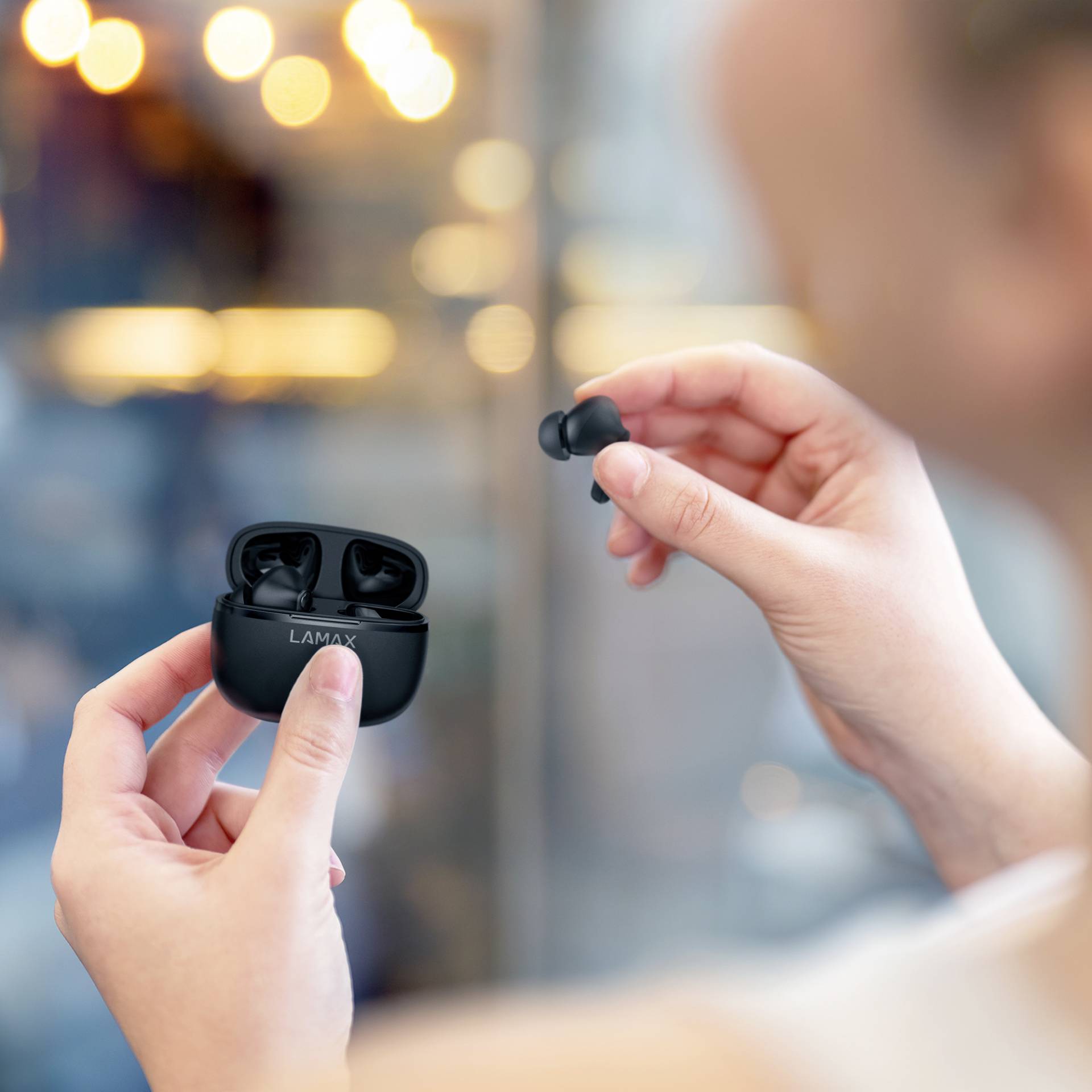 A person is holding wireless black earbuds and a charging case in their hands, ready to insert an earbud.