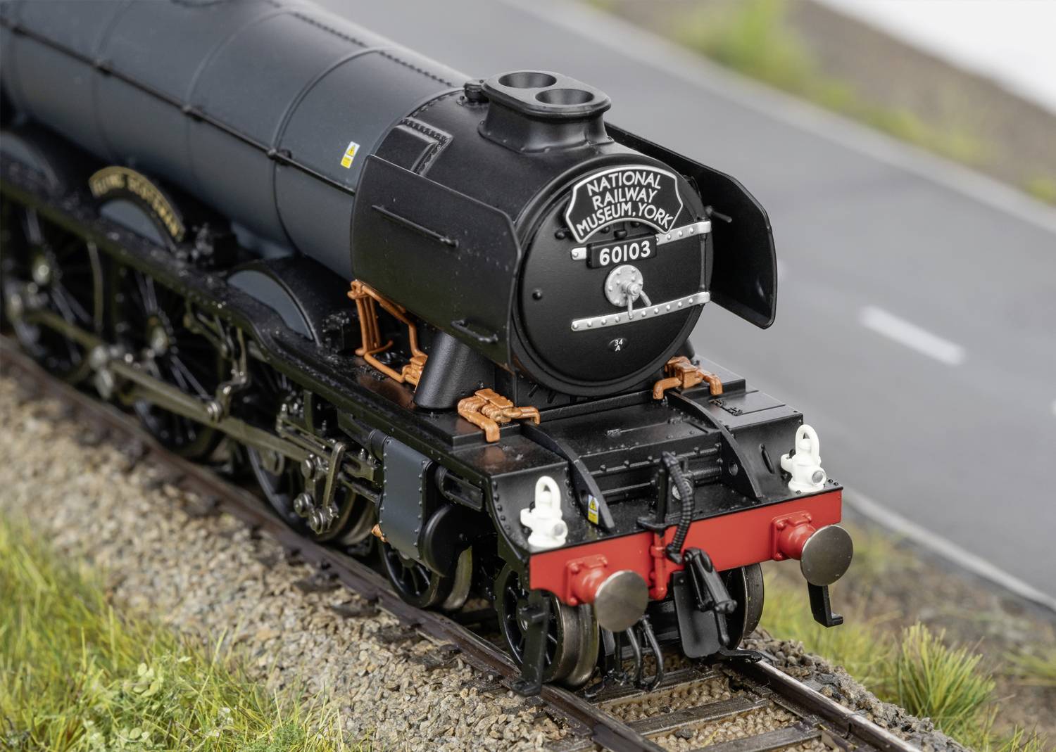 Model railway locomotive 60103 Flying Scotsman on tracks, with inscription 'National Railway Museum York', surrounded by grass.