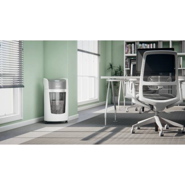 An office with pale green walls and large windows. A modern air purifier stands in the corner, surrounded by grey office chairs and a desk.