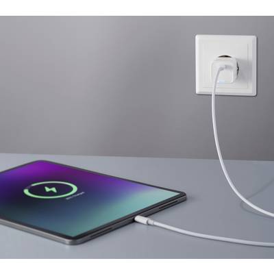 A tablet is lying on a table, connected to a charging cable plugged into a power socket. The screen displays a charging symbol.