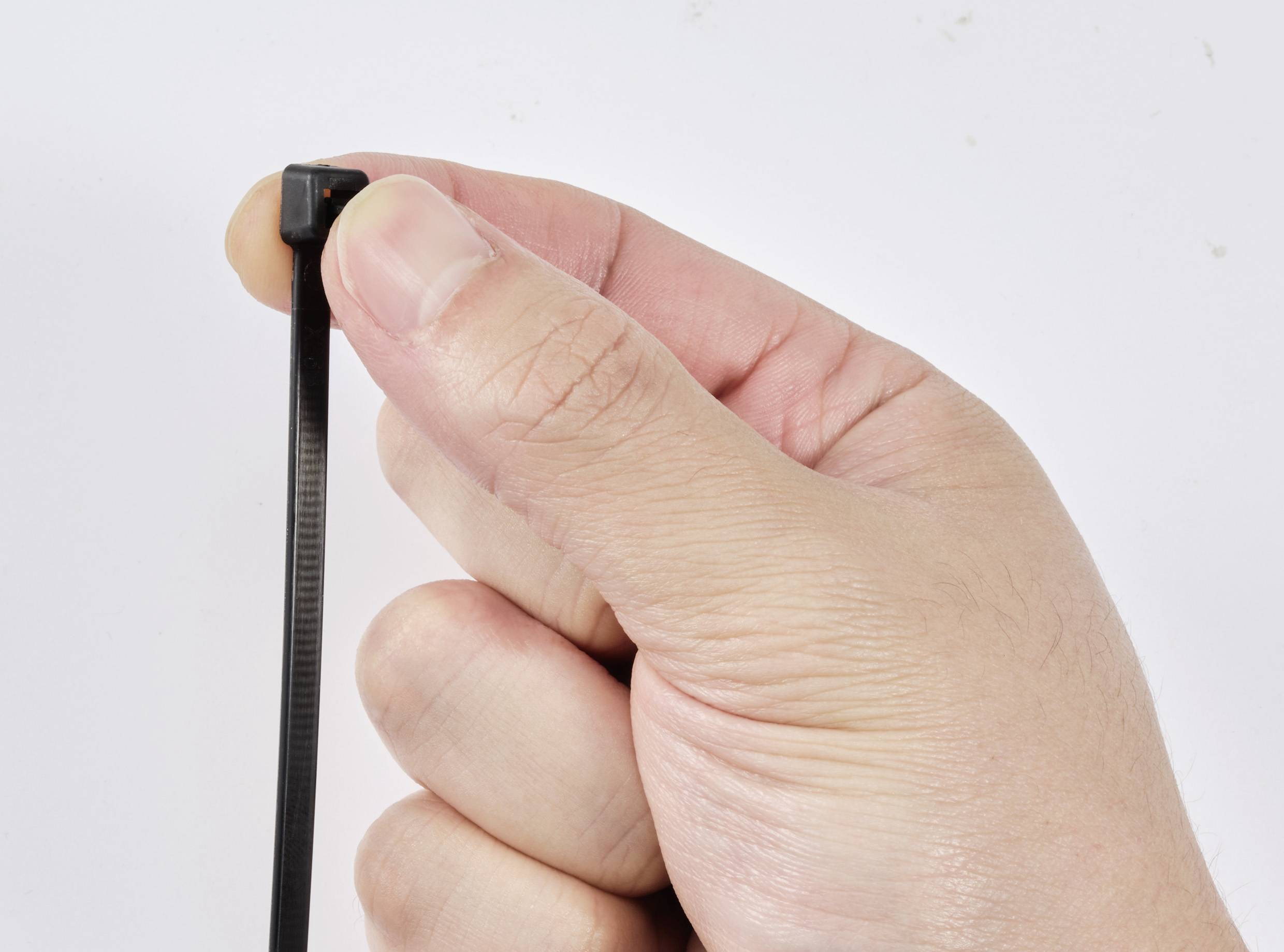 A hand holds a black cable tie against a white background.