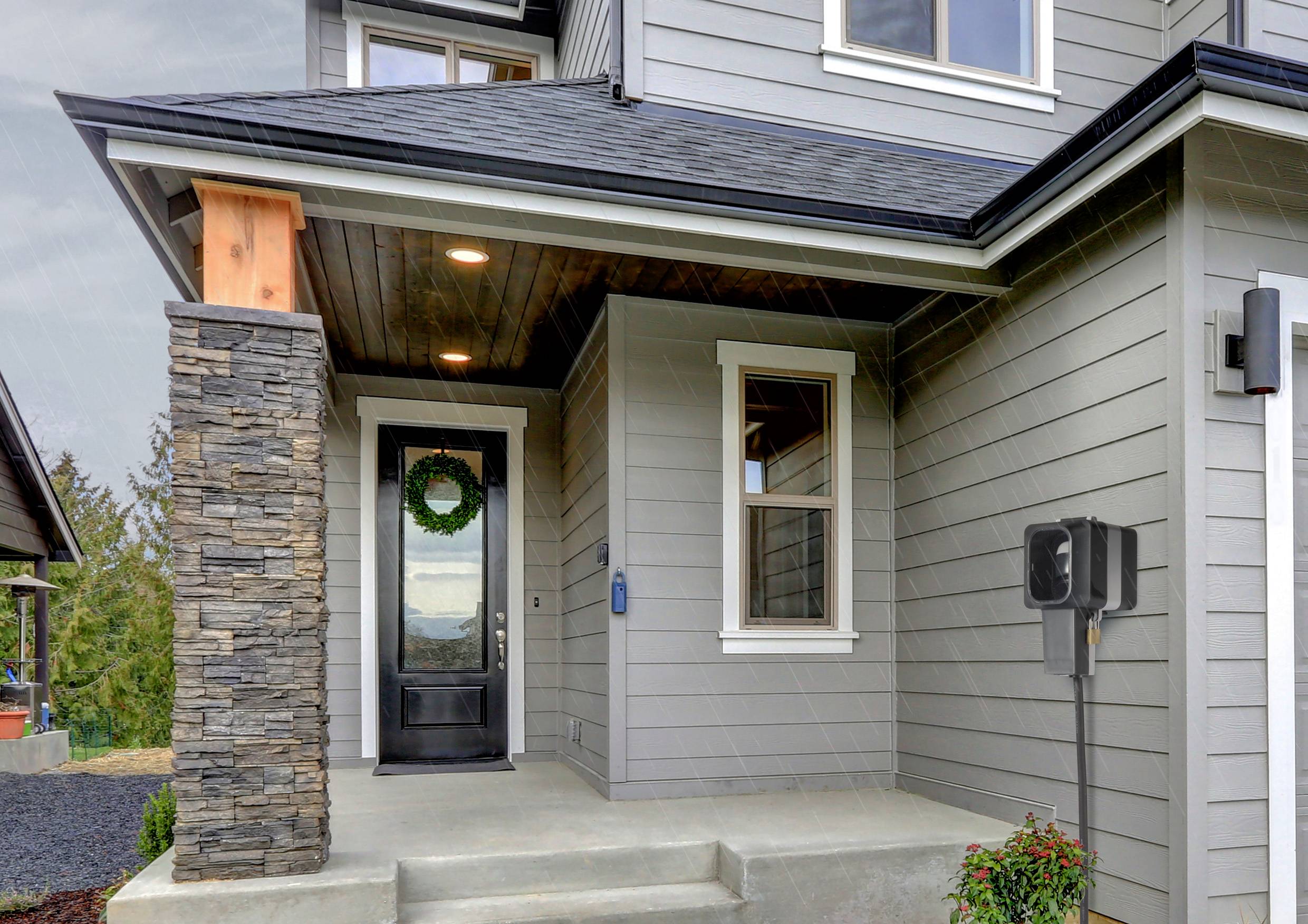 Entrance of a modern house with a grey wooden façade. A wreath decoration hangs on the black front door, with a charging station to the right.