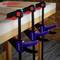 'Three black and red G-clamps are holding a wooden board to a table. The 'WORKPRO' logo is visible on the clamps.'