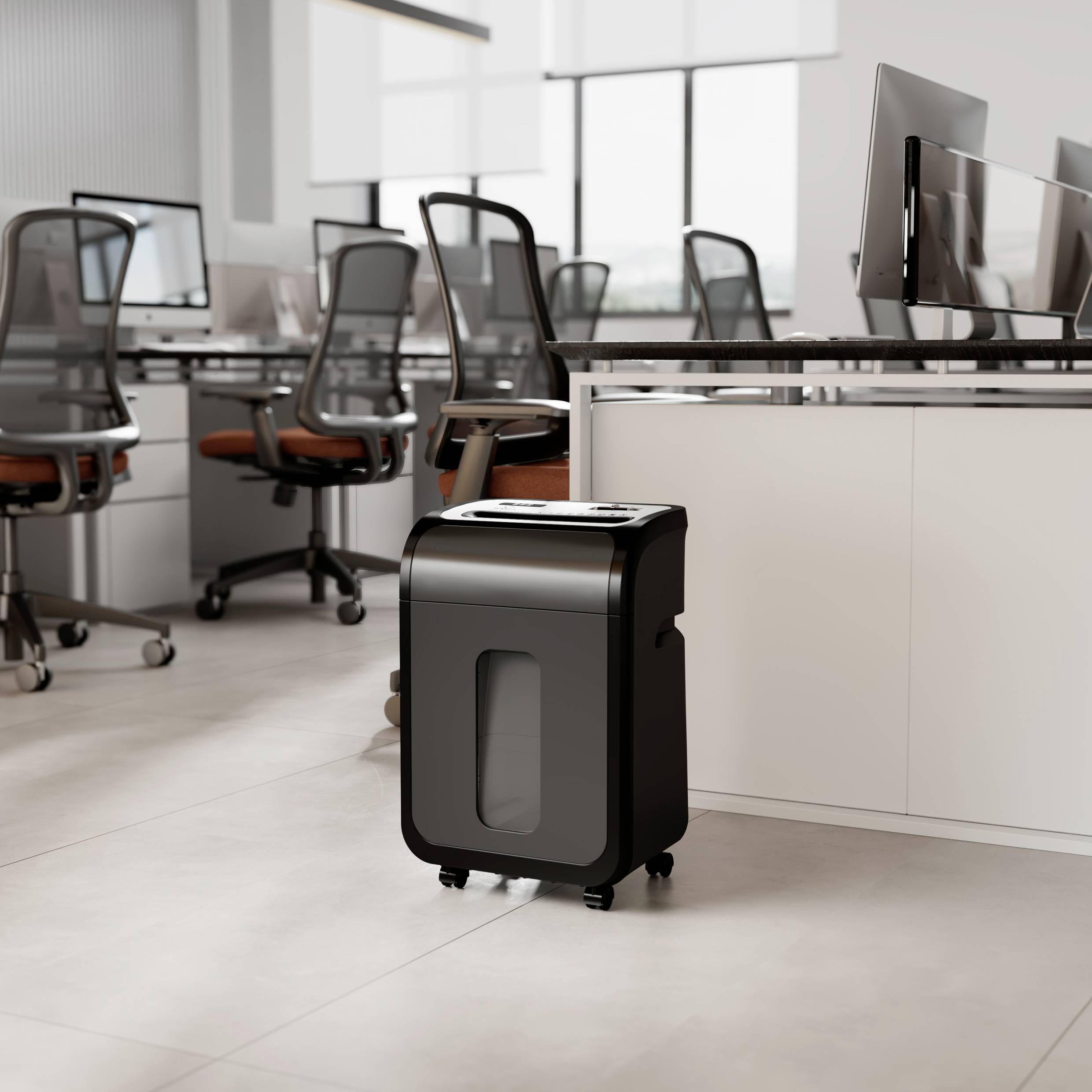 A paper shredder stands in a modern office with several office chairs and computers on white desks.