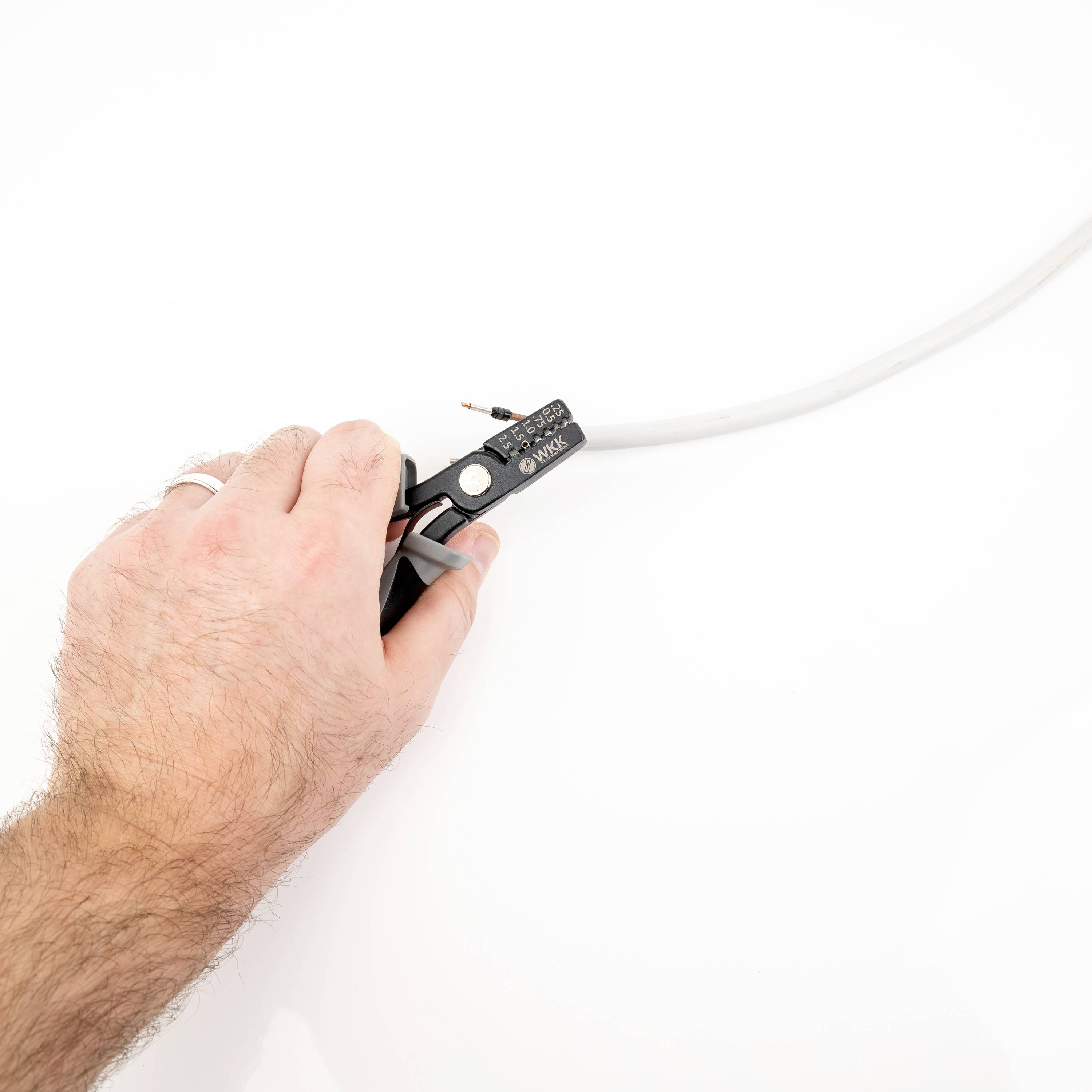 A hand is holding a wire stripper to remove the insulation from a white cable.