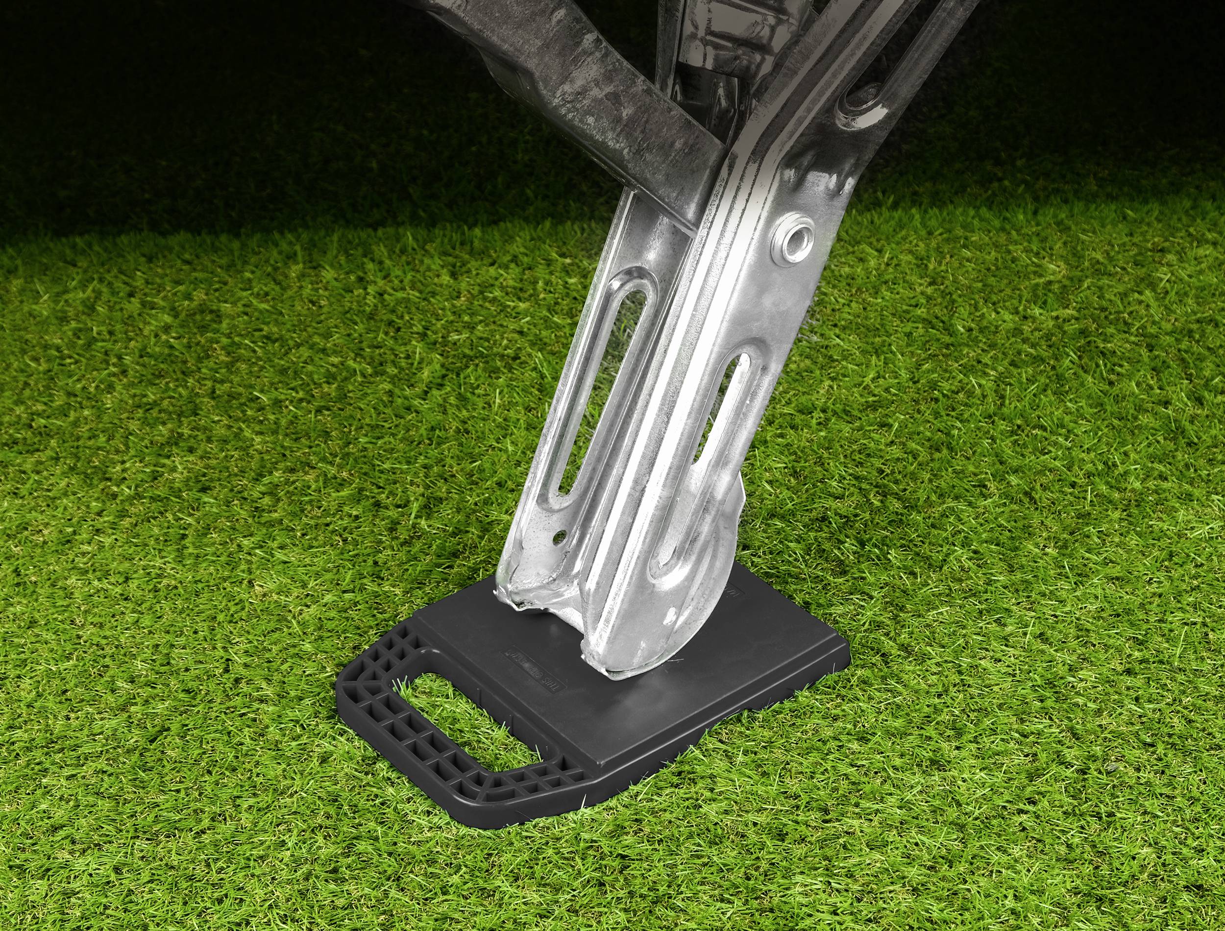 'A jack lifts a vehicle on a patch of green grass. The jack is standing on a stable, black base.'