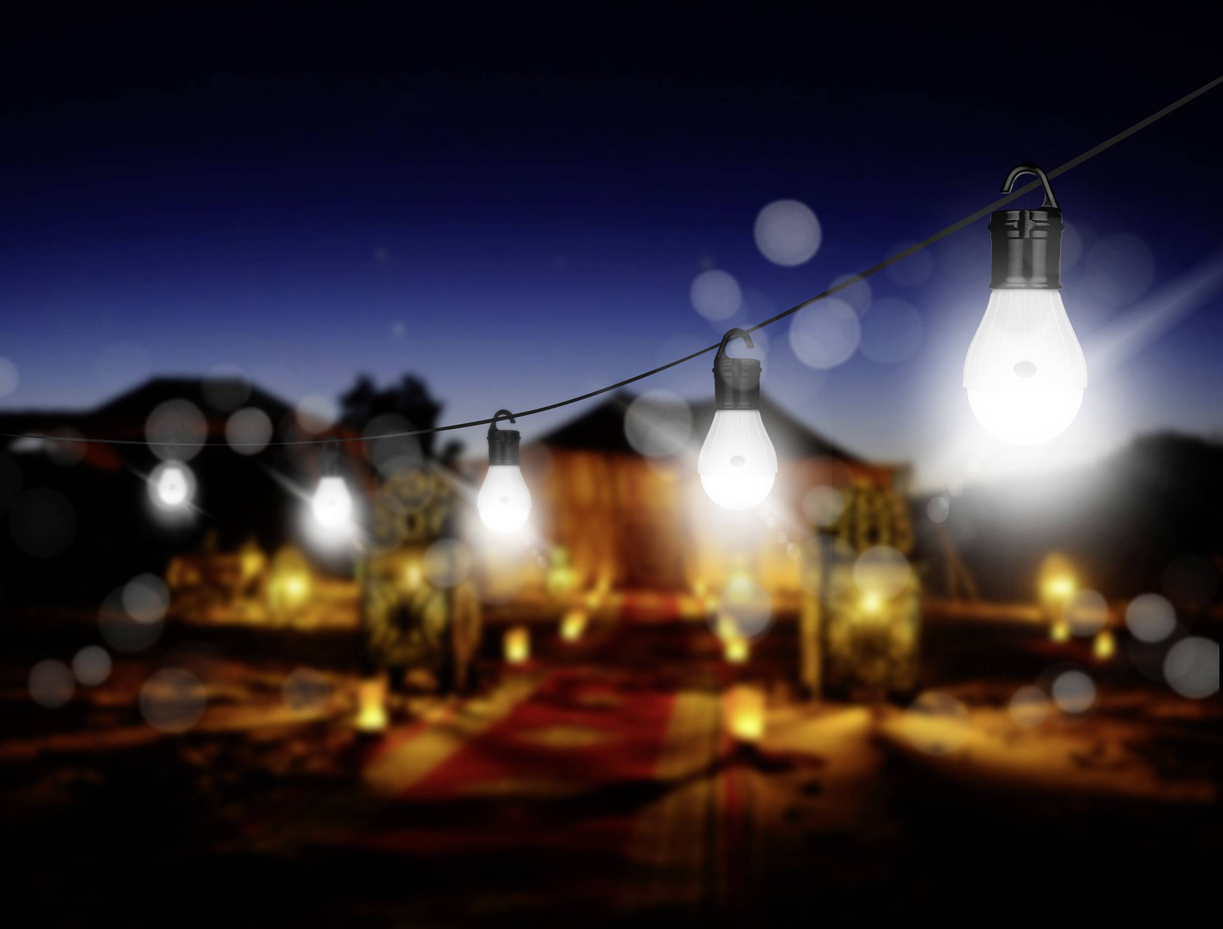 A row of glowing light bulbs hangs over a dimly lit outdoor area at dusk, creating a warm and inviting atmosphere.