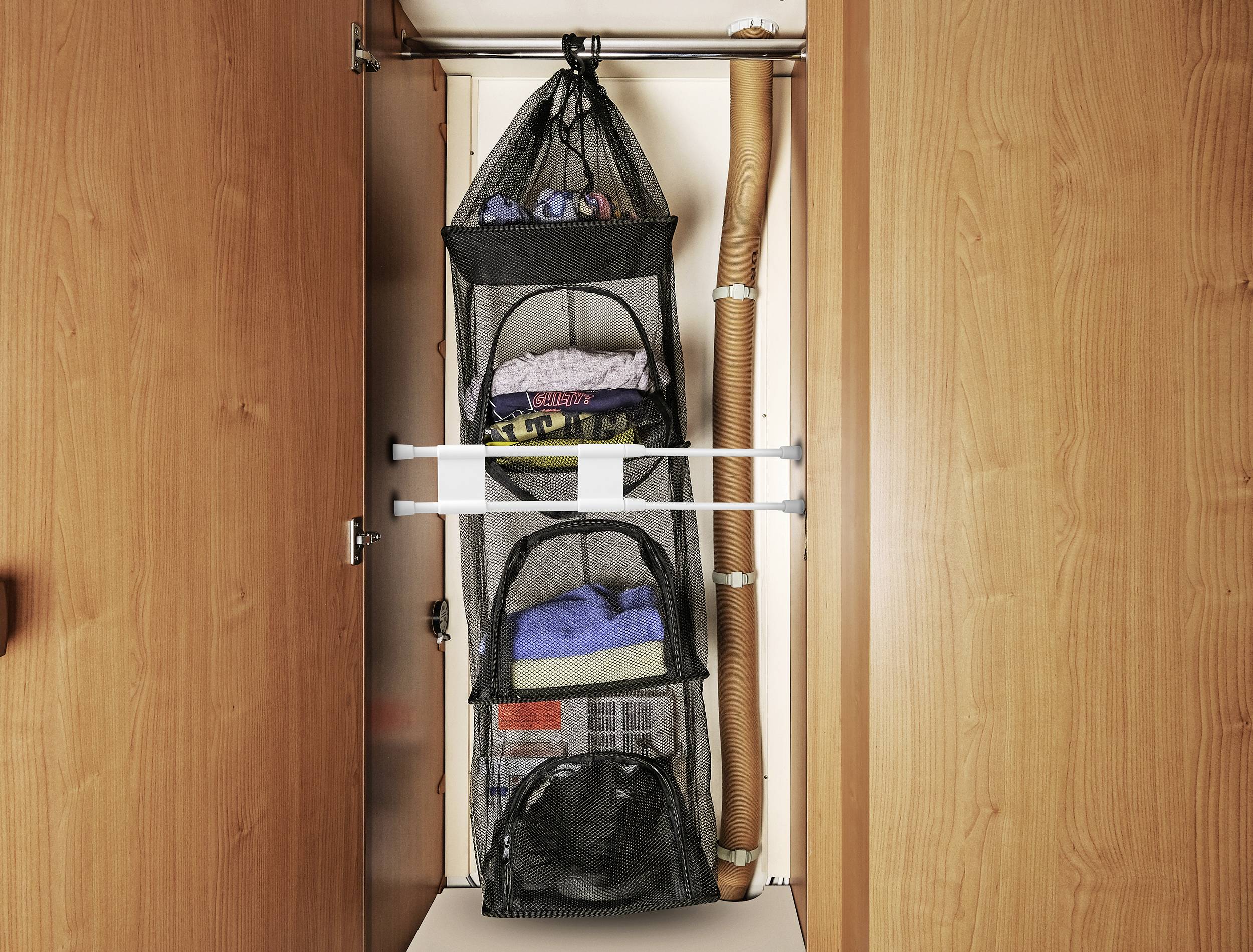 A wardrobe with open doors reveals a black, hanging mesh shelving unit with multiple compartments, filled with folded clothing items.