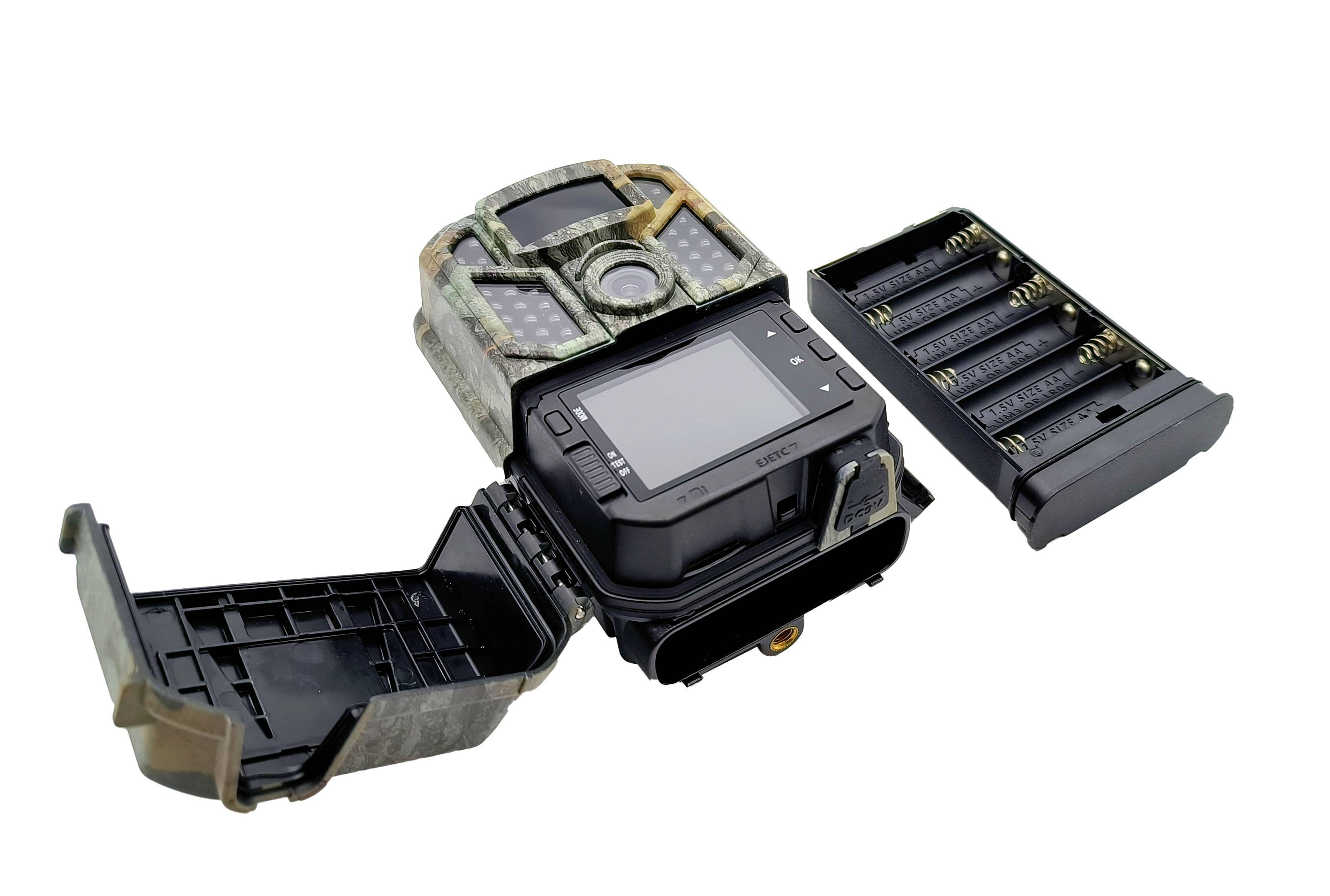 An open trail camera in camouflage colours displays the LCD screen and battery compartment with AA batteries.