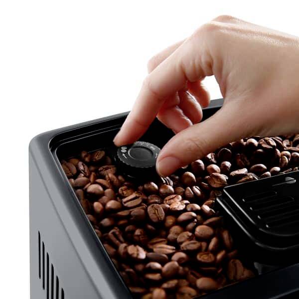 A hand holds a magnet over a box of coffee beans to remove metal fragments.