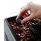 A hand holds a magnet over a box of coffee beans to remove metal fragments.