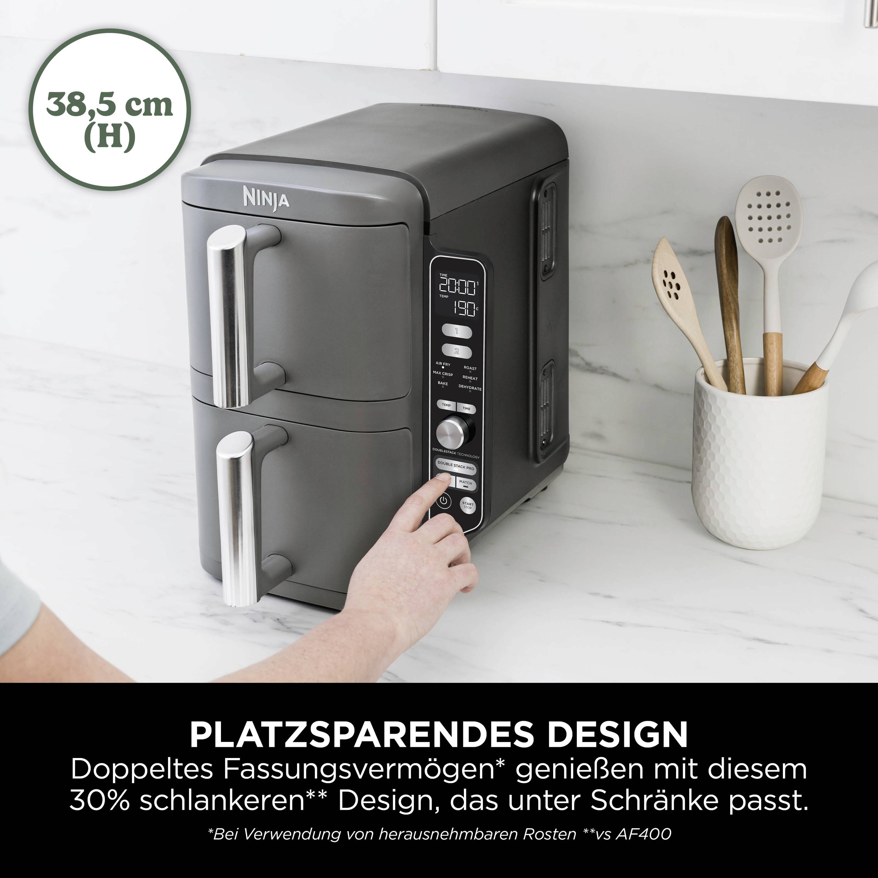 A person's hand selects a setting on a compact, black air fryer situated on a white work surface.