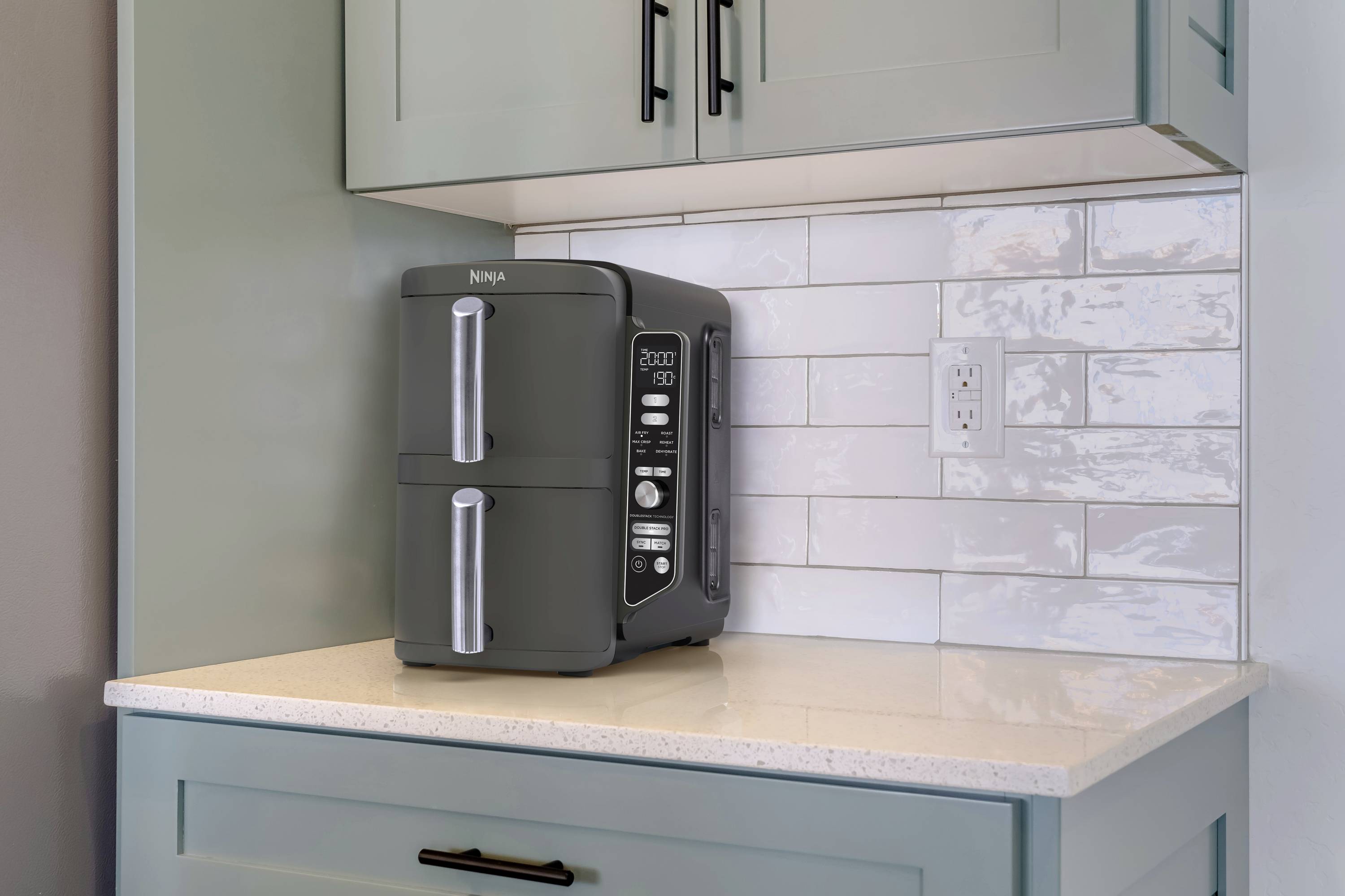 A deep fat fryer sits on a kitchen worktop in front of a tiled wall. The digital display shows the time.