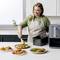 A woman serves baked food from an air fryer onto plates with green beans, in a modern kitchen.