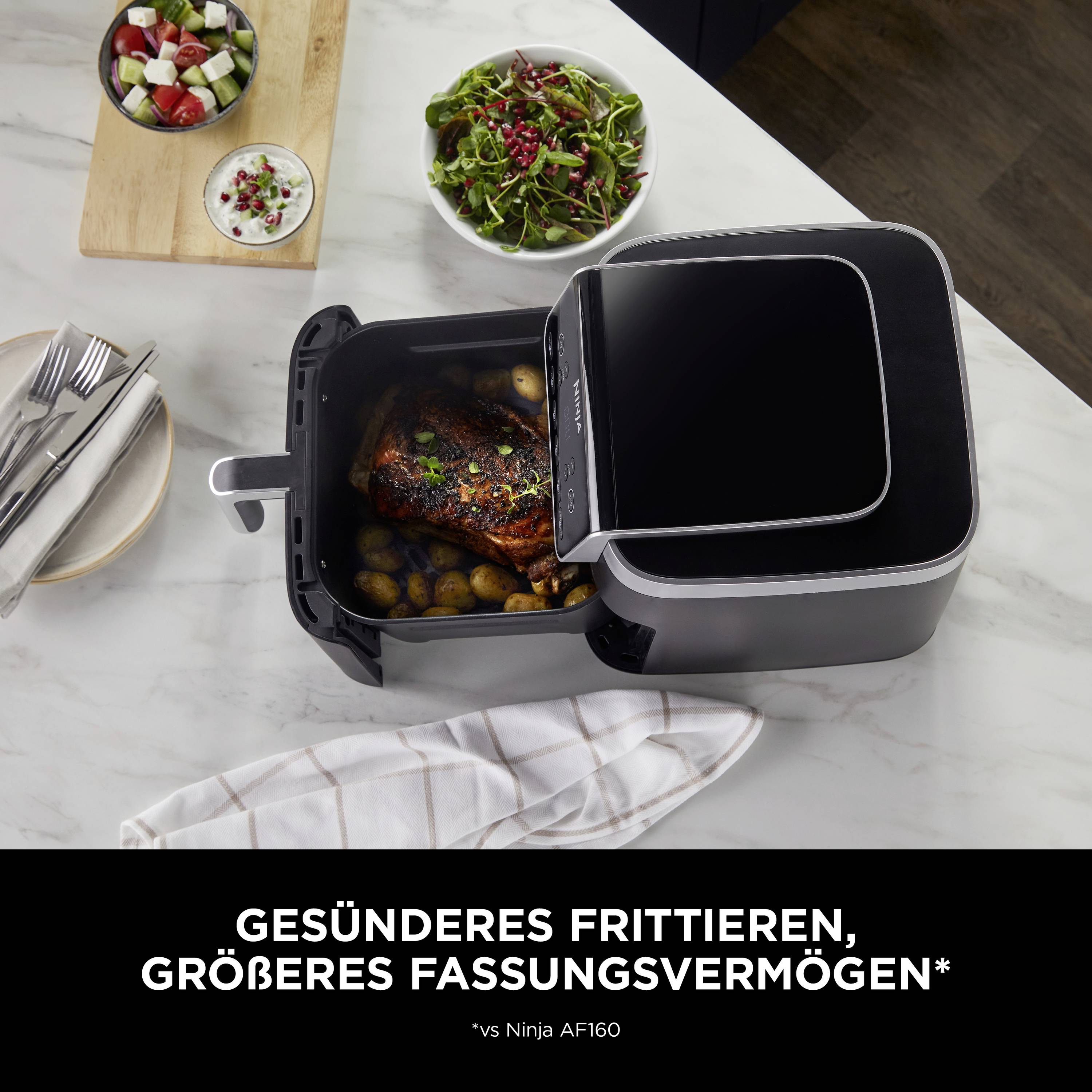 'Air fryer on kitchen table with chicken and potatoes, surrounded by side dishes in bowls. Text: Healthier frying, larger capacity.'