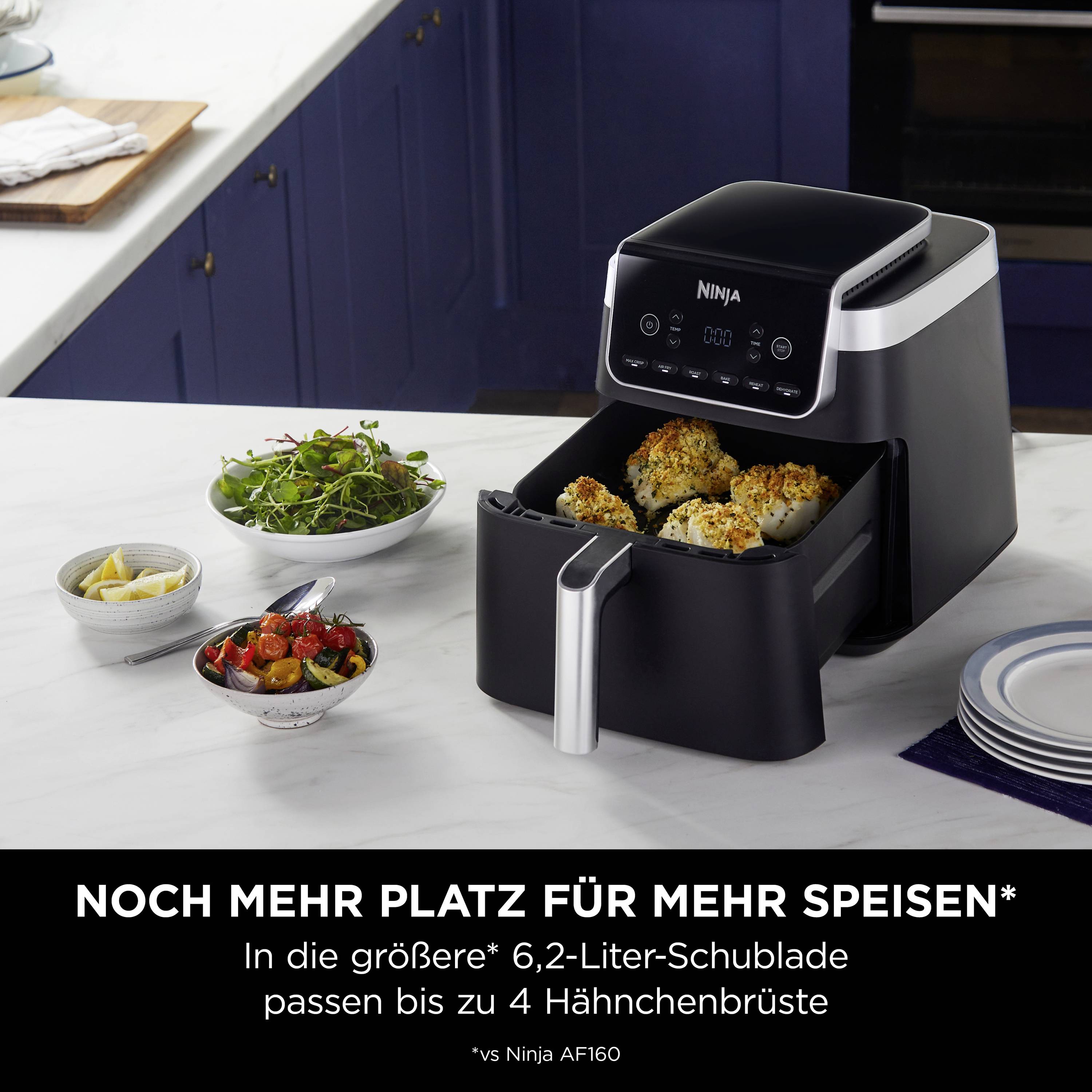 A black air fryer with an open drawer containing four golden-brown pieces of chicken sits on a kitchen worktop.