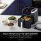 A black air fryer with an open drawer containing four golden-brown pieces of chicken sits on a kitchen worktop.