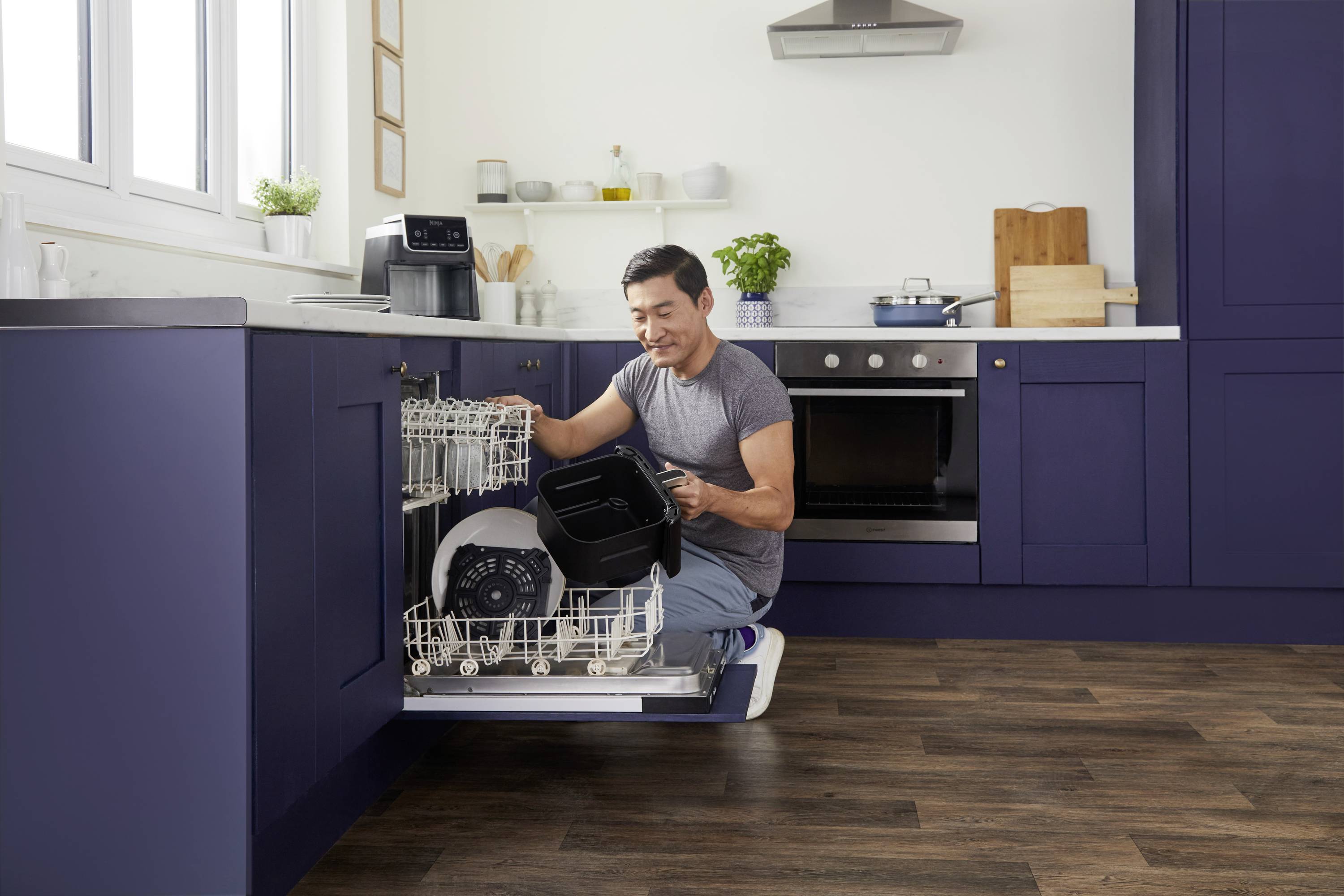 A man is loading a dishwasher in a modern kitchen. A coffee machine sits on the worktop.