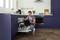A man is loading a dishwasher in a modern kitchen. A coffee machine sits on the worktop.