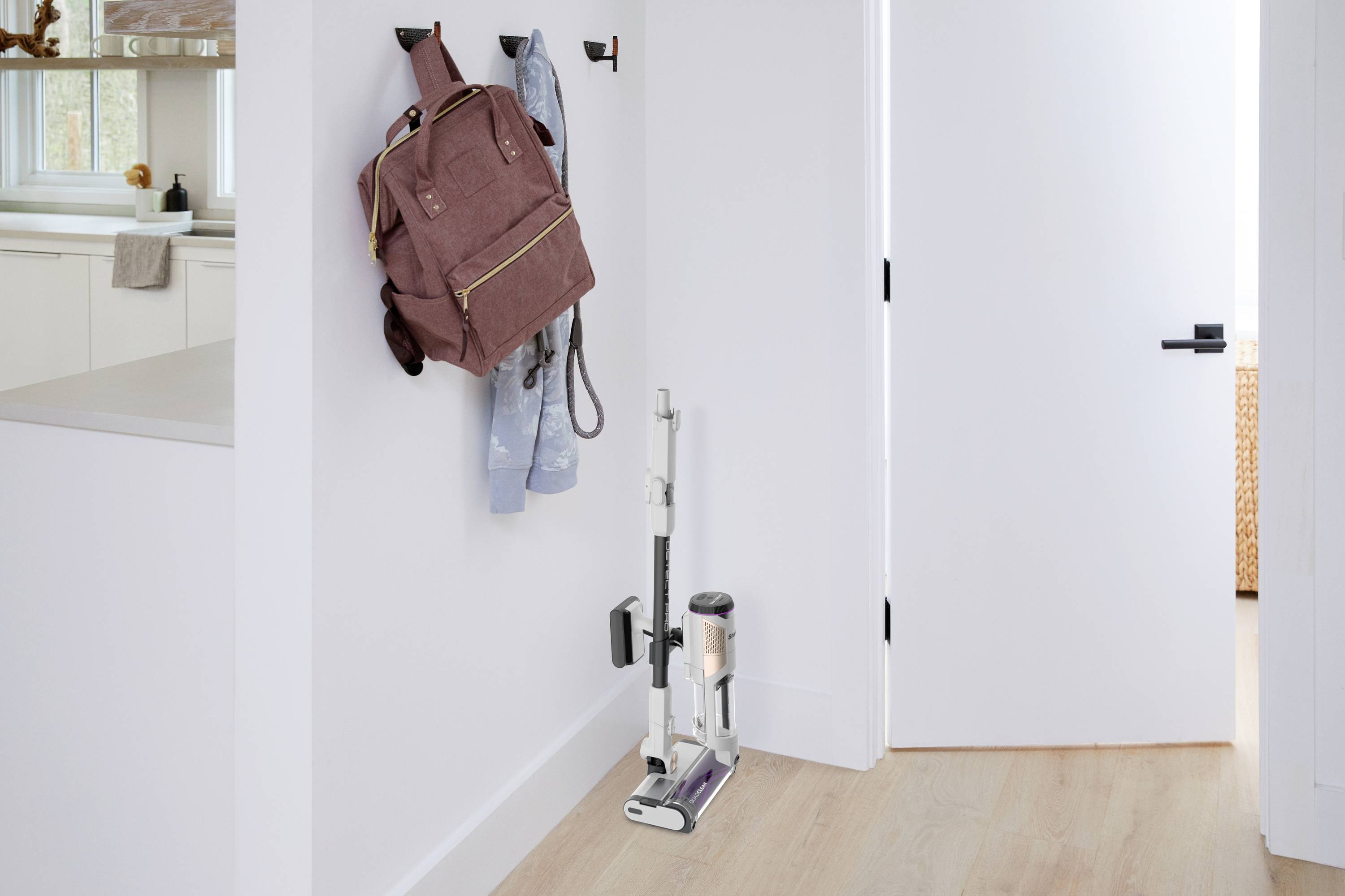 A vacuum cleaner stands in a corridor next to an open door. A rucksack and a jacket are hanging on the wall.