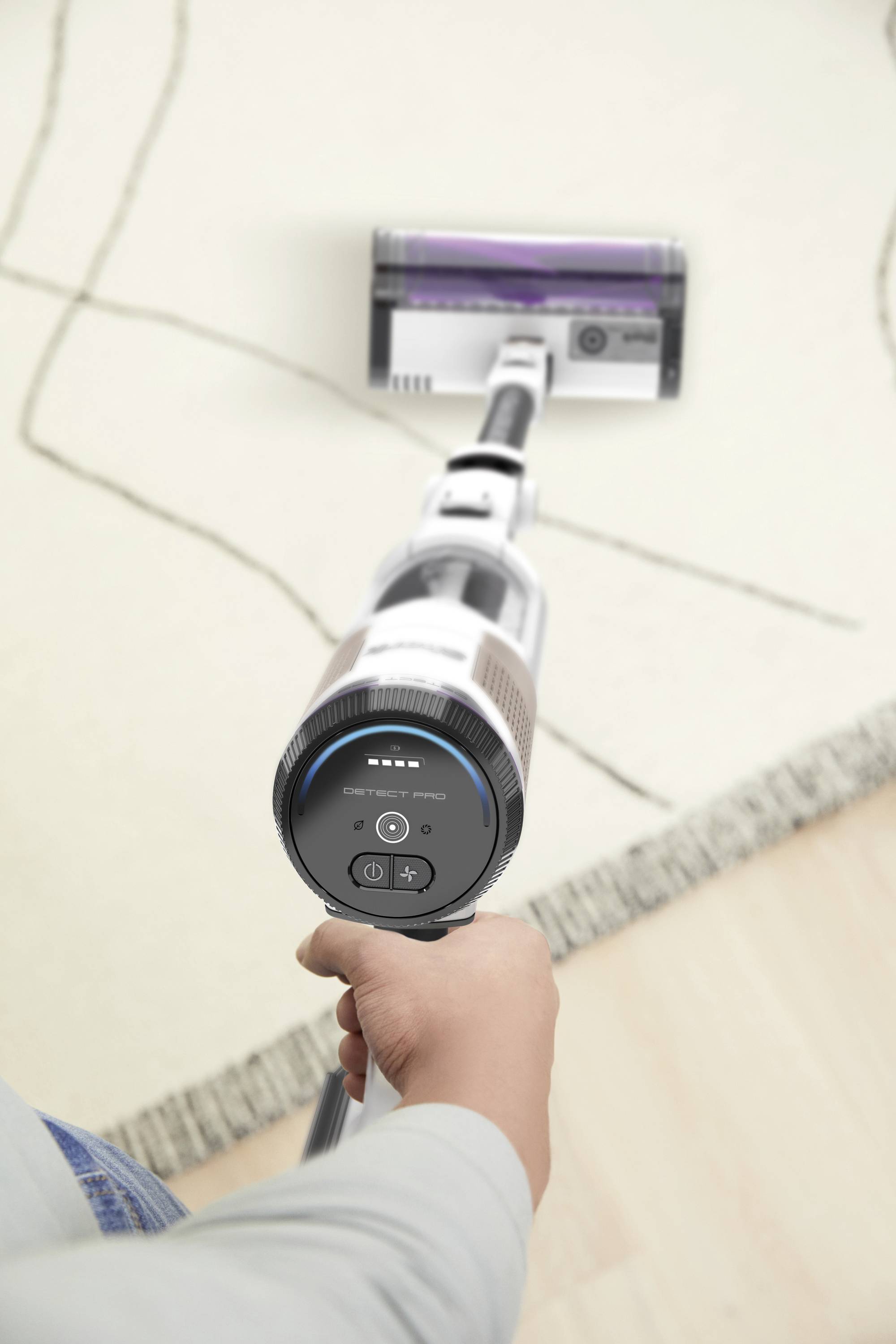 A person is holding a vacuum cleaner and cleaning a carpeted floor. The focus is on the vacuum brush and the clean carpet.
