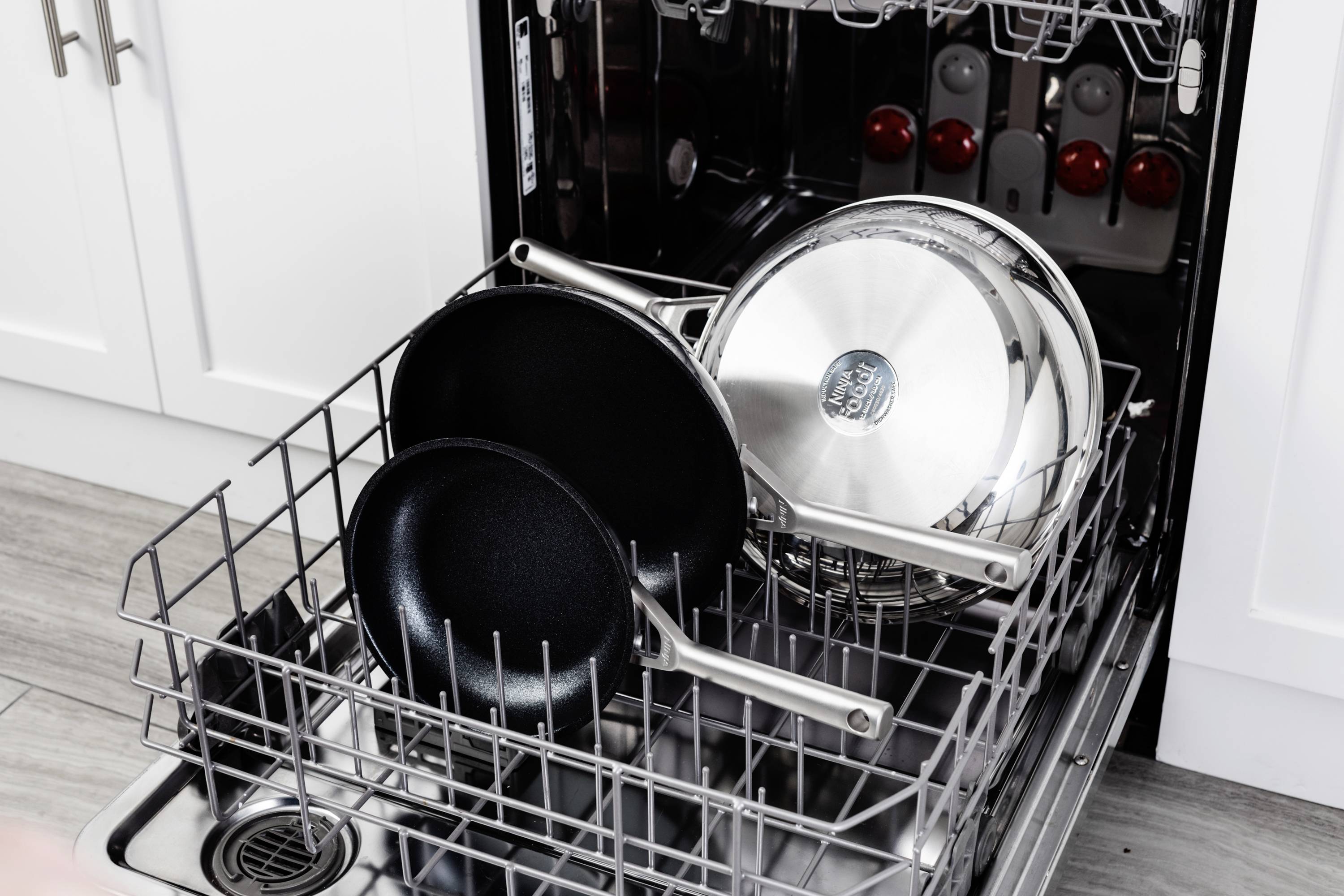 Open dishwasher with several black and silver pans in the bottom rack, ready to be washed.