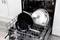 Open dishwasher with several black and silver pans in the bottom rack, ready to be washed.